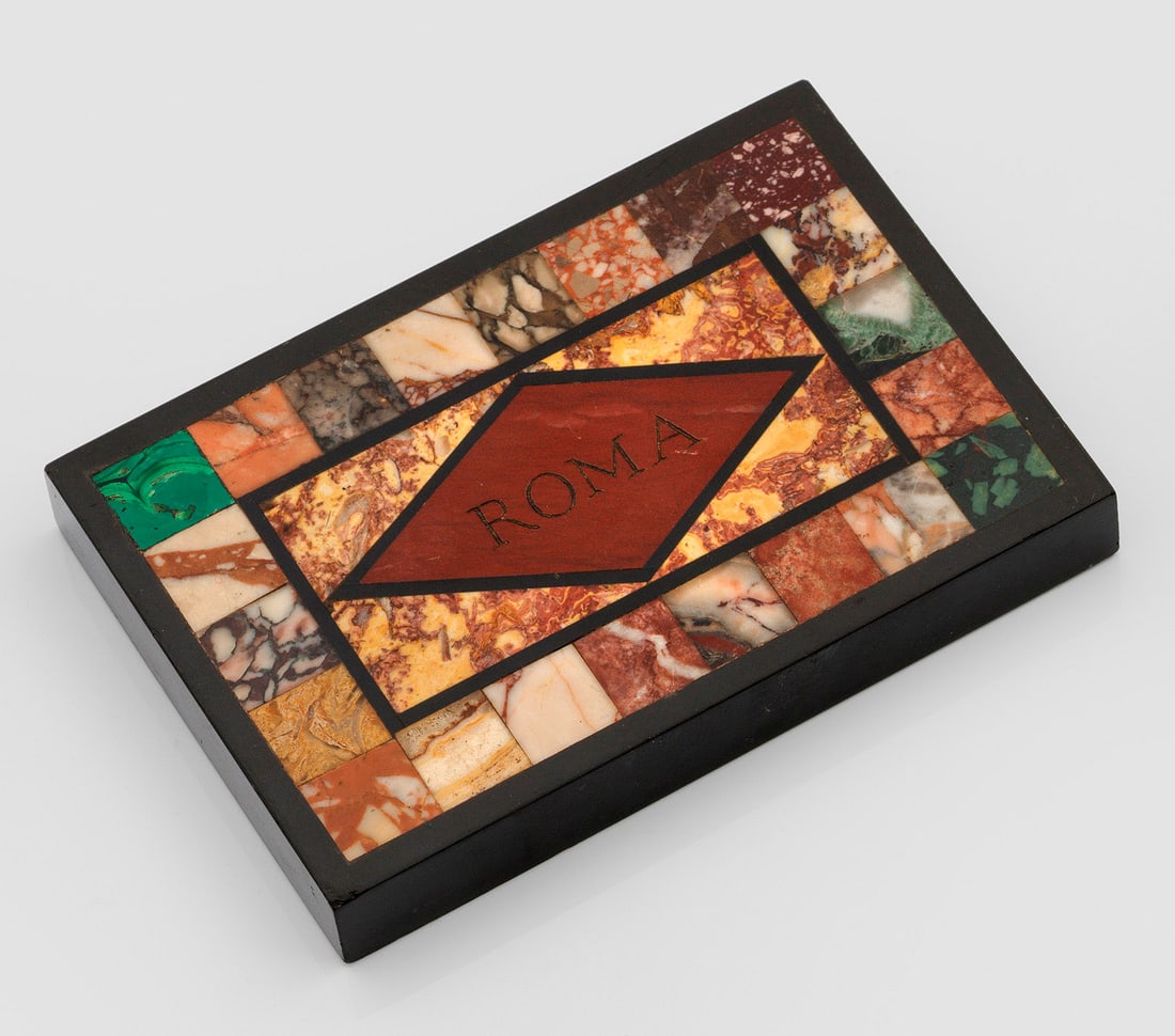 Pietra Dura-Briefbeschwerer: Marmor. In schwarzer Marmorrahmung verschiedene eingelegte Ornamente aus farblich unterschiedlichem Marmor. Mittig graviert "Roma". 8 cm x 12 cm. An Italian marble Pietra Dura paperweight, engraved at