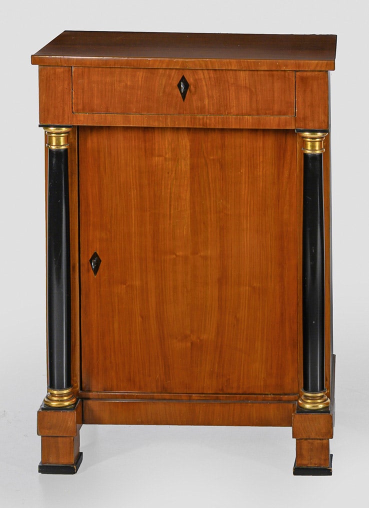 Biedermeier-Konsolschrank: Kirschbaum, furniert und teilw. ebonisiert. Gerader, hochrechteckiger Korpus auf schmaler Zarge und gekanteten Füßen. In der gegliederten Front eine Tür, flankiert von eingestellten Säulen als St�