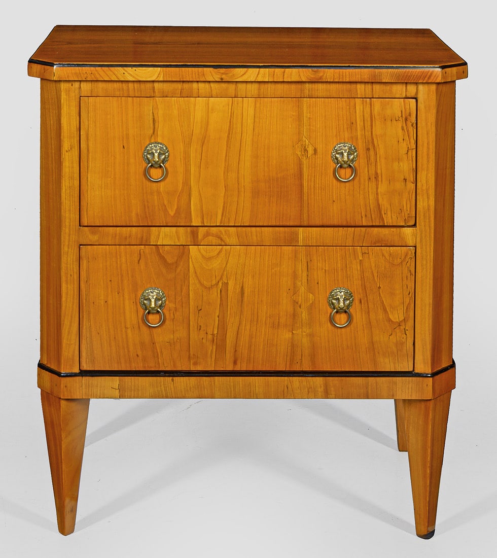 Biedermeier-Pfeilerkommode: Kirschbaum, furniert und teilw. ebonisiert. Gerader, hochrechteckiger Korpus, flankiert von schmalen, schräggestellten Ecklisenen auf flacher Zarge und gekanteten Vierkantbeinen. In der gegliederten 