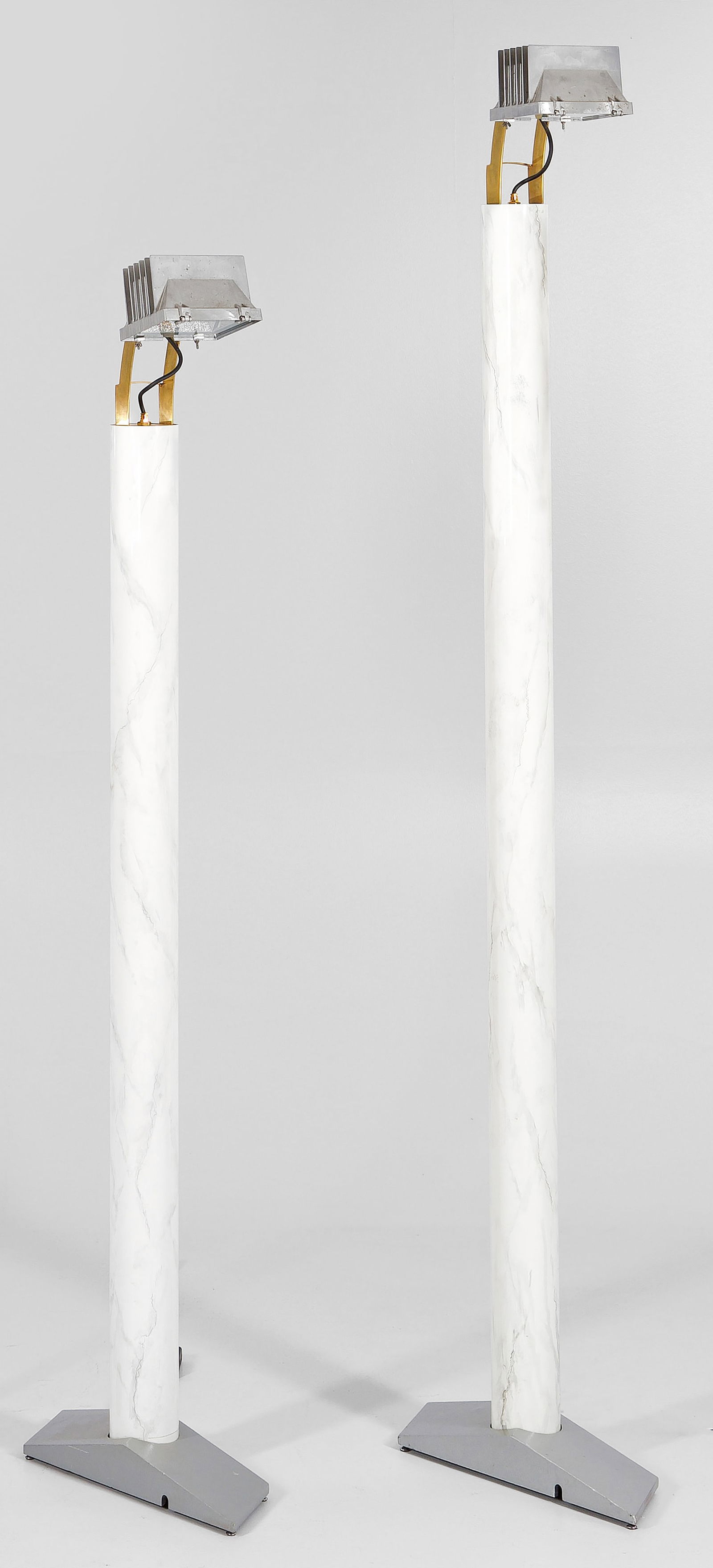 Zwei große Bodenlampen "Kohlmarkt" von Hans Hollein: 1-flg.; Messing, Gusseisen und Metall, teilw. cremefarben in Marmoroptik emailliert. Über schräg ansteigender Basis hoher, zylinderförmiger Schaft als Träger für Leuchtmittel in Form eines Strahl