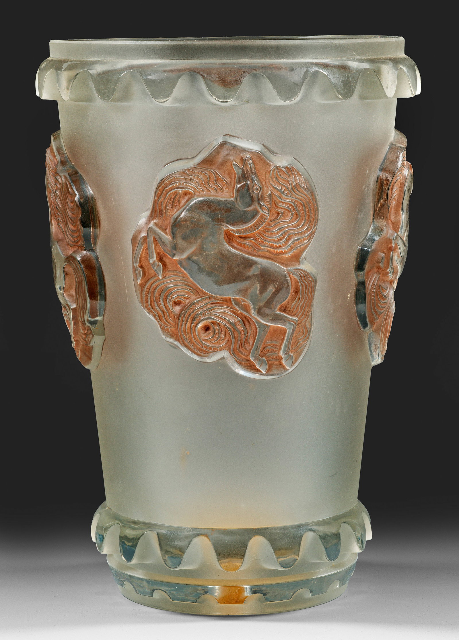 Lalique-Vase "Carmague": Sich leicht konisch erweiternde Becherform. Farbloses, in die Form geblasenes, teilw. bräunlich patiniertes, satiniertes bzw. poliertes Glas, der Rand geschliffen. Reliefplastischer Dekor aus vier gr