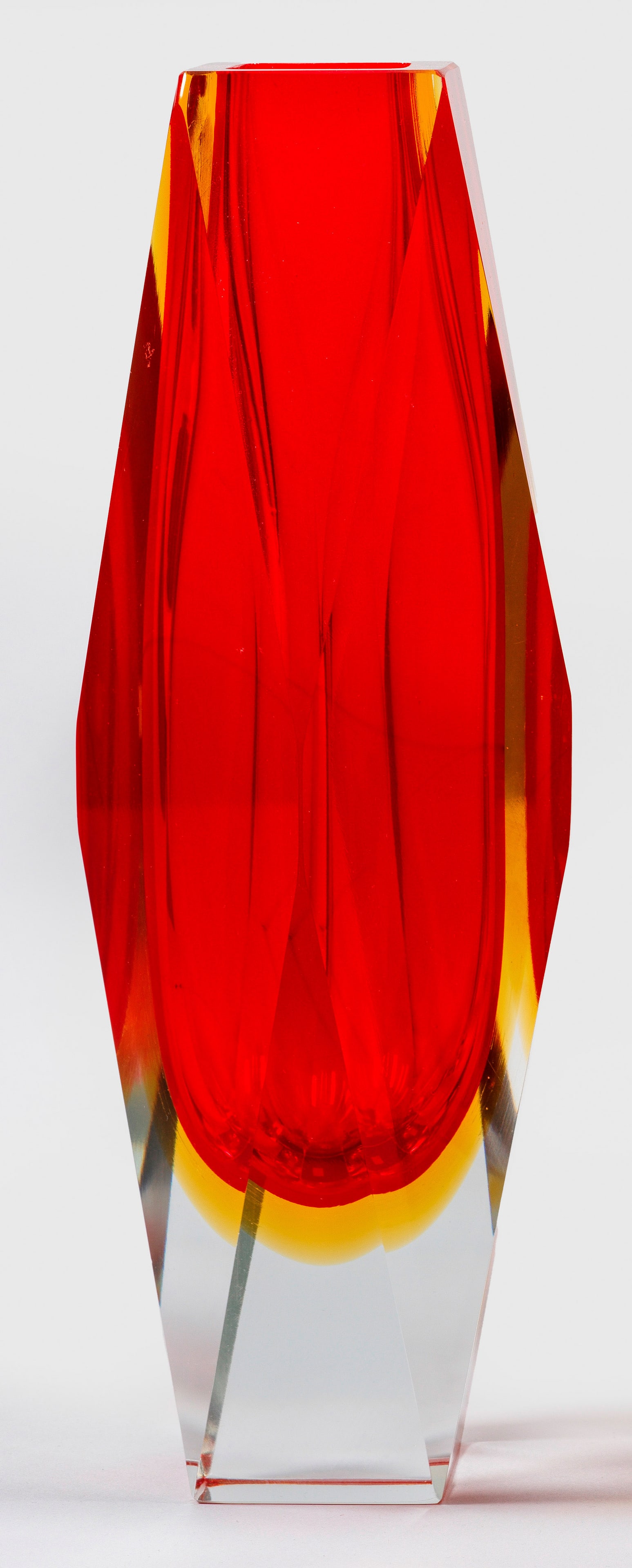 Murano-"Sommerso"-Vase im Sixties-Design: Schlanke, stereometrische Polyeder-Form mit quadratischem Stand und Lippenrand, die Seiten aus Dreiecks- und Rautenflächen. Dickwandiges Überfangglas, farblos, feuerrot und gelb, facettiert geschlif