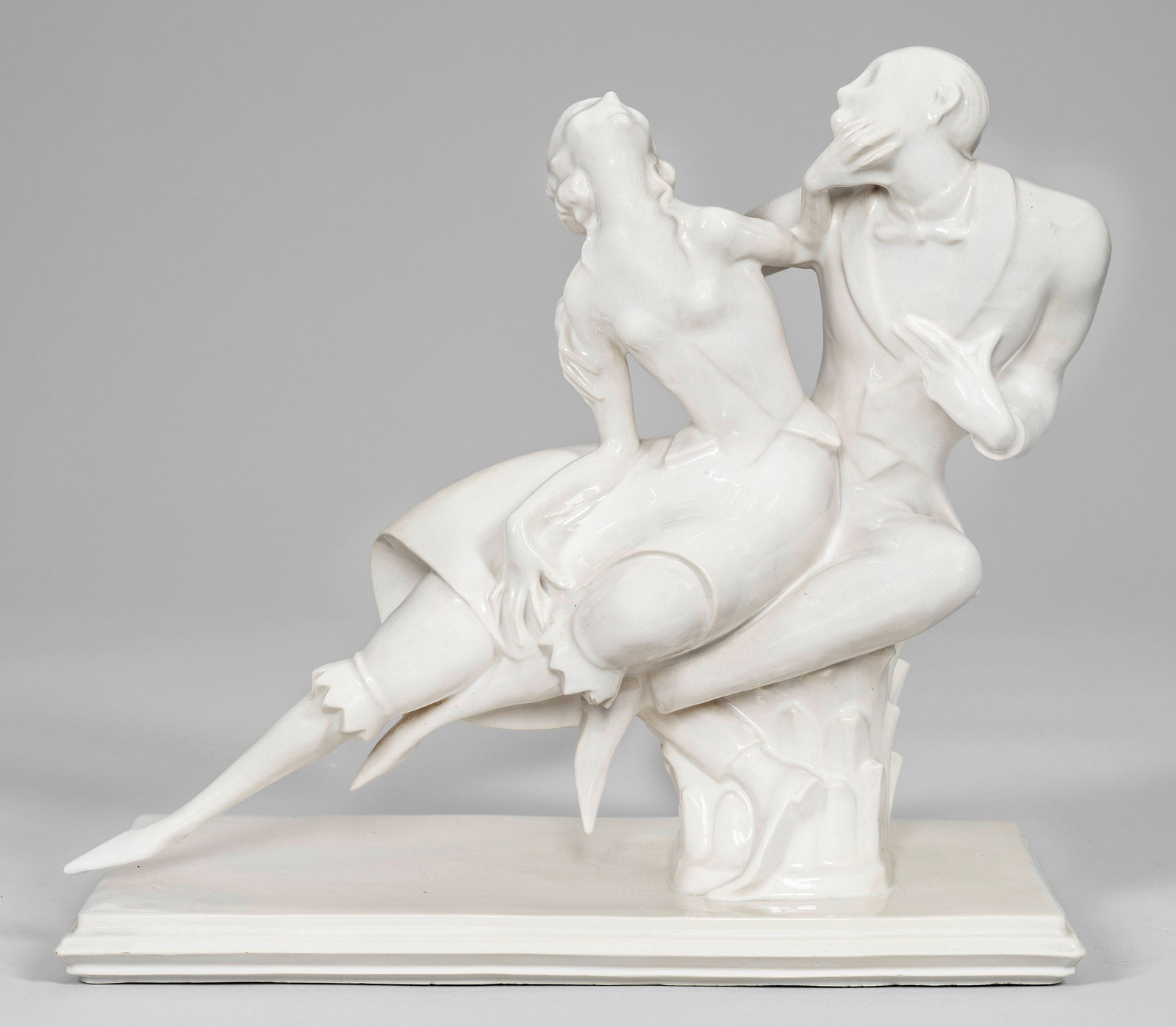 Art Déco-Tanzgruppe: Fayence, altweiß glasiert. Auf profilierter Rechtecksplinthe Dame und Herr in eng verschlungener Tanzpose. Entw. Emil Sutor. Geprägte Manufakturmarke. Unw. rest.; H. 30,5 cm x 34 cm x 17,5 cm. Ein V