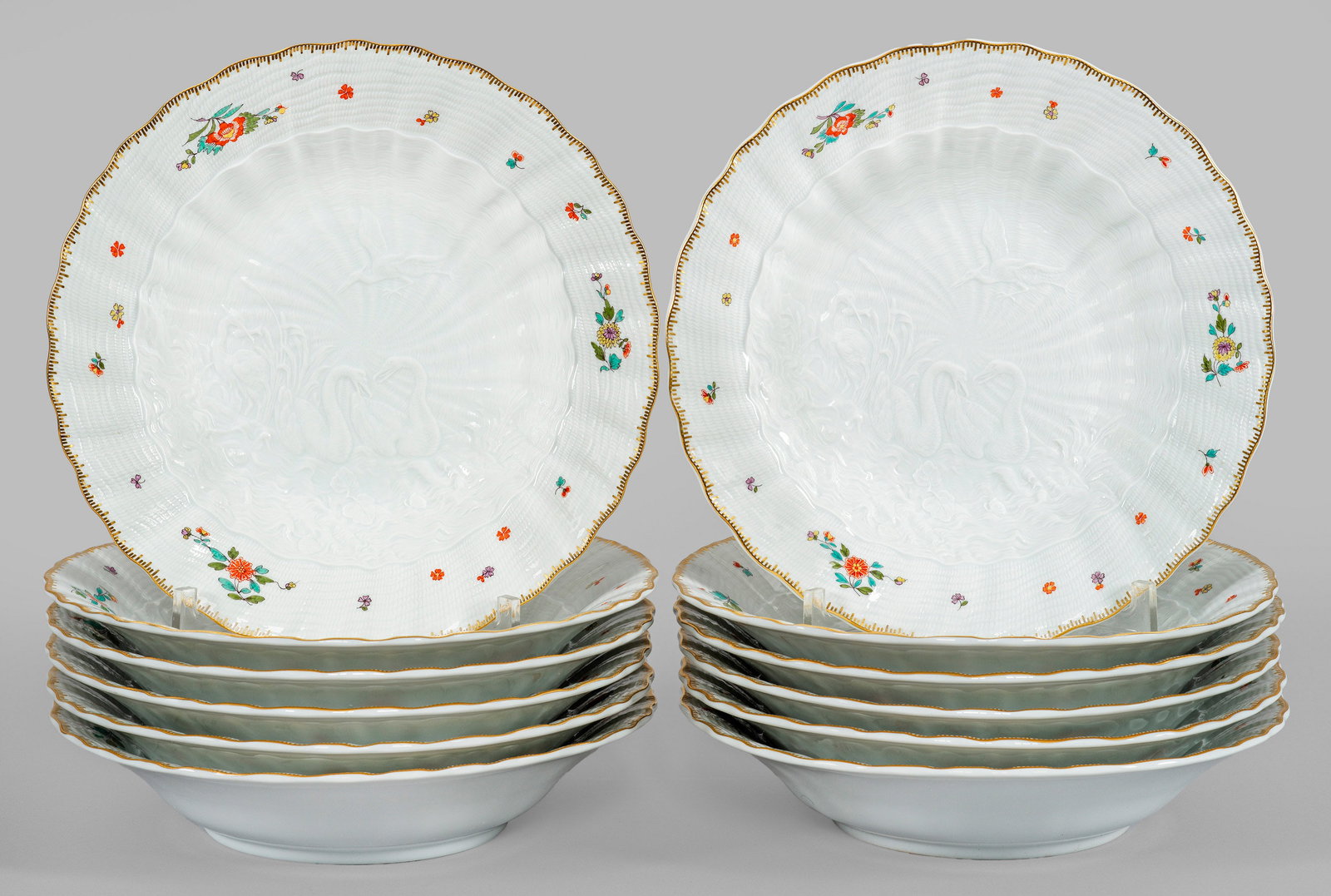 Zwölf Suppenteller mit Schwanenservice-Dekor: Runde Form. Feiner, muschelförmiger Reliefdekor aus dem Schwanenservice (Schwanendessin). Im leicht vertieften Spiegel zwei auf dem Wasser schwimmende, einander zugewandte Schwäne zwischen hohem Sch