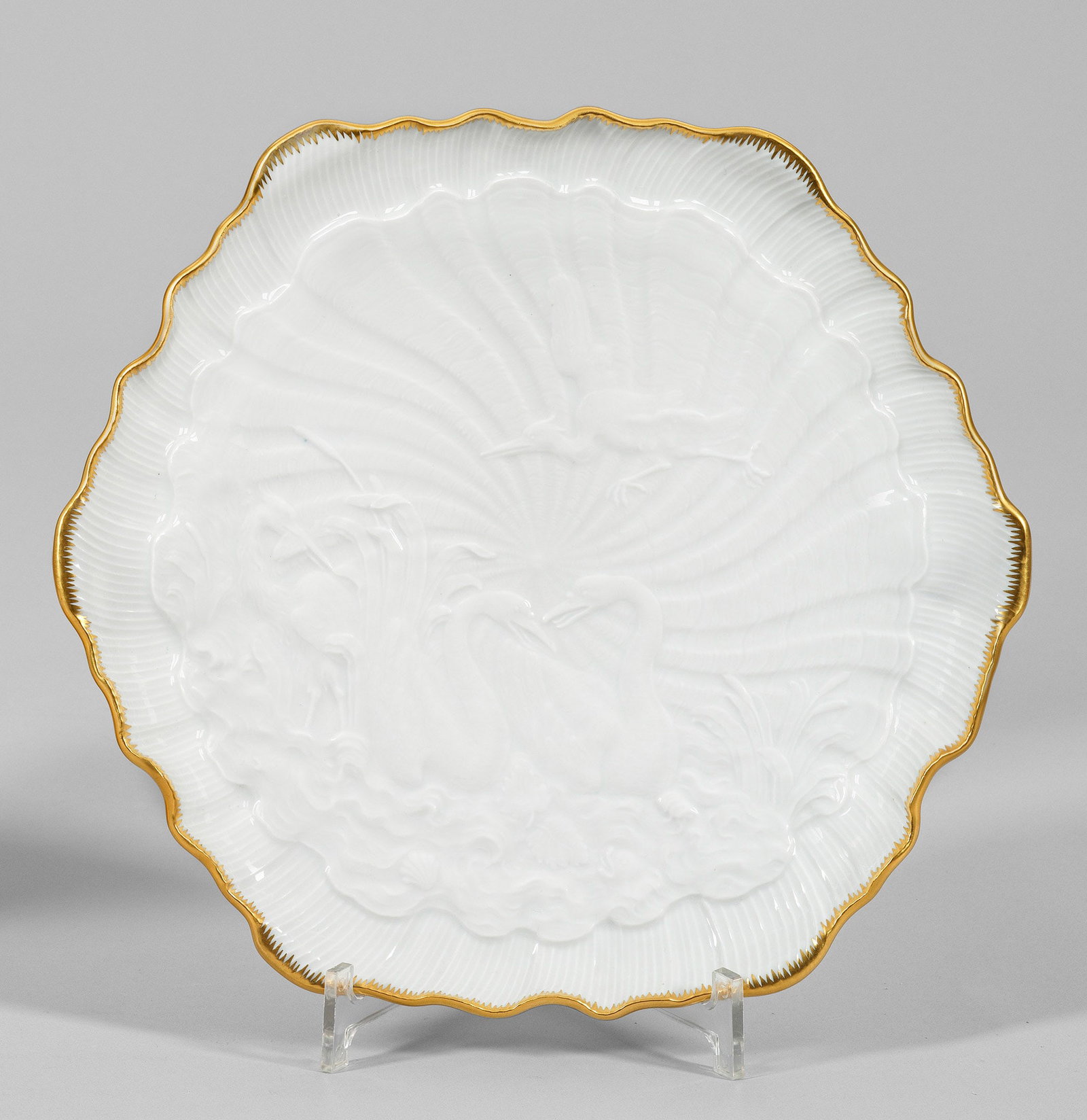 Gebäckplatte mit Schwanenservice-Dekor: Runde, passig geschweifte, flach gemuldete Form. Im Spiegel feiner muschelförmiger Reliefdekor (Schwanendessin) aus zwei einander zugeneigten Schwänen, fliegendem und zwischen hohem Schilf stehendem