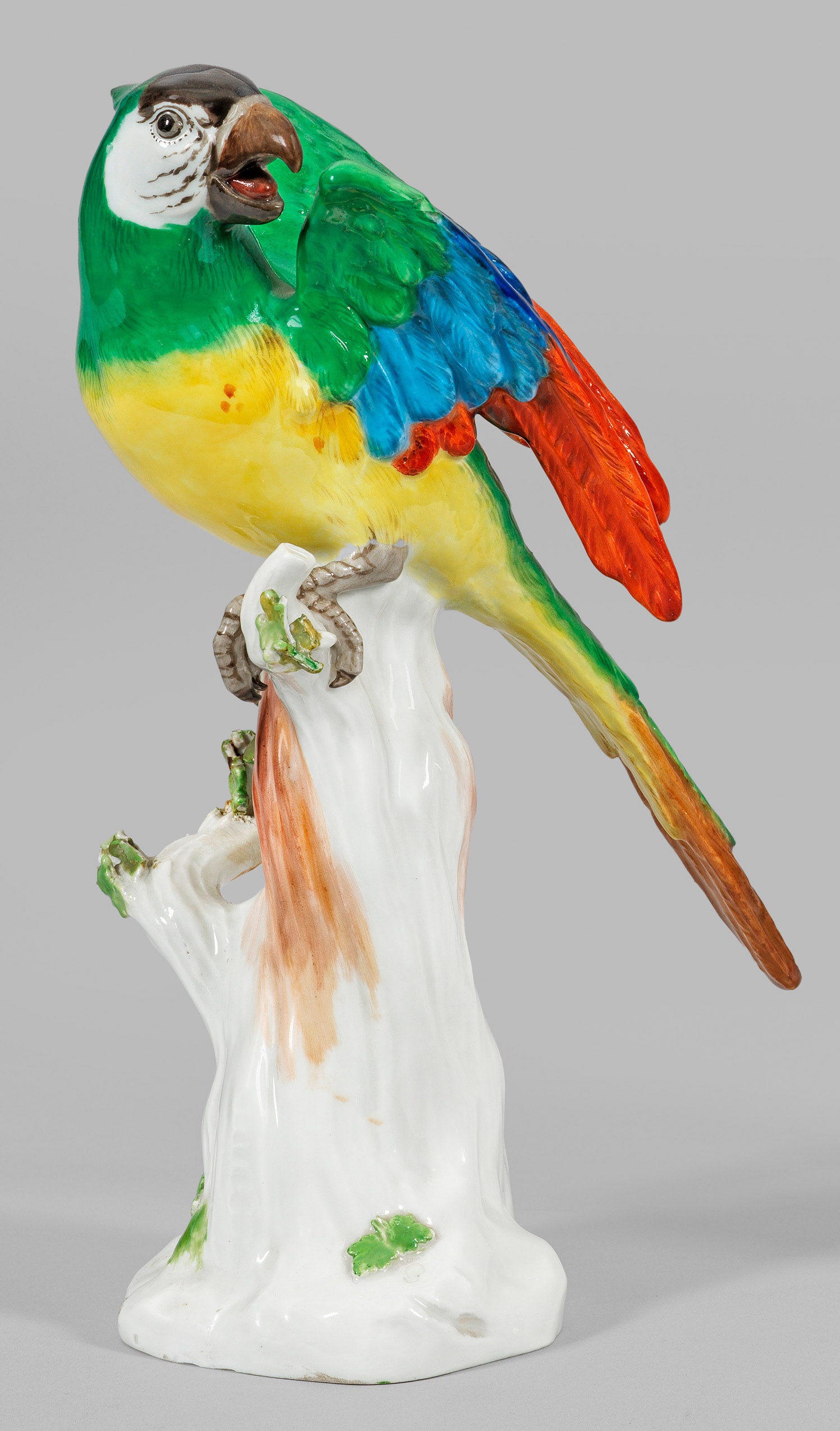 Papagei auf Stamm: Auf Felssockel emporragender Baumstamm mit plastischen Blättern. Darauf sitzender Papagei mit reliefiertem, farbenprächtigem Federkleid. Polychrome Malerei. Entw. Johann Joachim Kaendler. Modell-Nr.