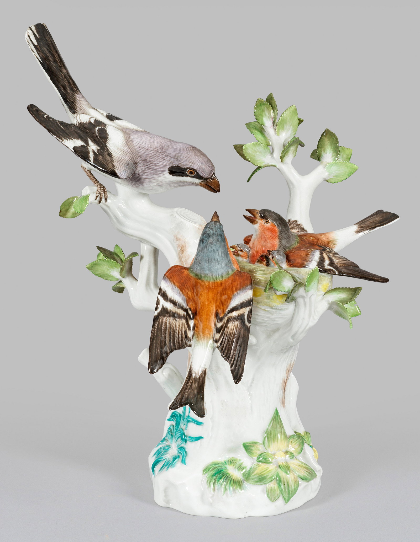 Vogelgruppe mit Finken und Sperber am Nest: Auf hohem, bewachsenem Baumstammsockel, zwischen emporragenden, sich verzweigenden Ästen, liegendes Vogelnest mit Buchfinkweibchen und ihren Jungen. Seitlich sitzendes Männchen bzw. herannahender Te