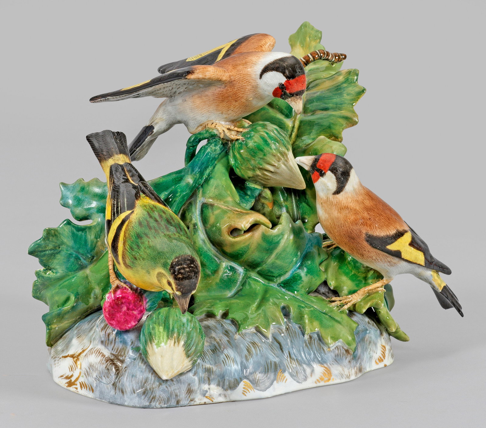 Distelfinkengruppe von Meissen: Auf rechteckig gerundetem Natursockel zwischen plastischen Distelblättern sitzende, sich den Knospen zuwendende Distelfinken. Auf einem Blatt eine kriechende Raupe. Polychrome Malerei mit Goldstaffag