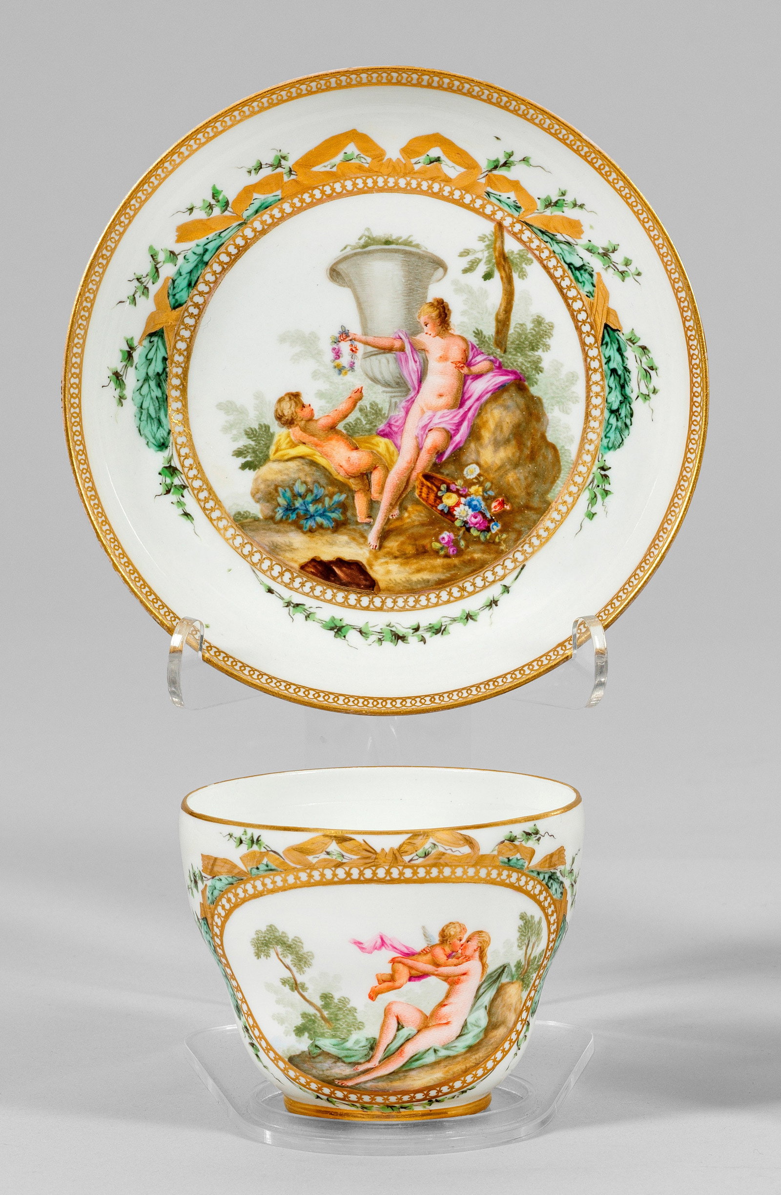 Feine Ziertasse mit Venus und Amor nach François Boucher: Über dem Rundstand halbkugelig, leicht gebuckelter Korpus, seitlich sich überkreuzender Bandhenkel in Blattrelief endend. Im von Efeu und Schleifen bekrönten Rund des Spiegels in Felsenlandschaft a