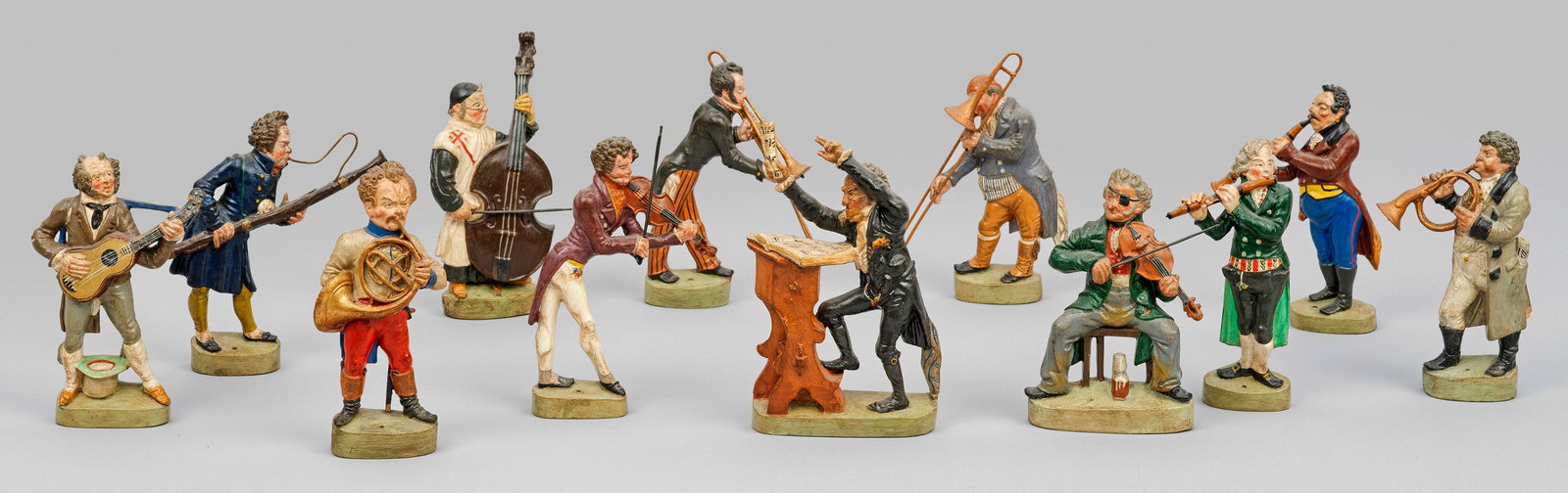 Zwölf Zizenhausener Figuren aus dem sog. "Großen Orchester": Terrakotta, polychrom bemalt. Instrumente mit Metalldetails. Auf länglich-ovaler Plinthe reliefplastisch gestaltete, rücks. abgeflachte, partiell ausgehöhlte Darstellungen des Dirigenten und