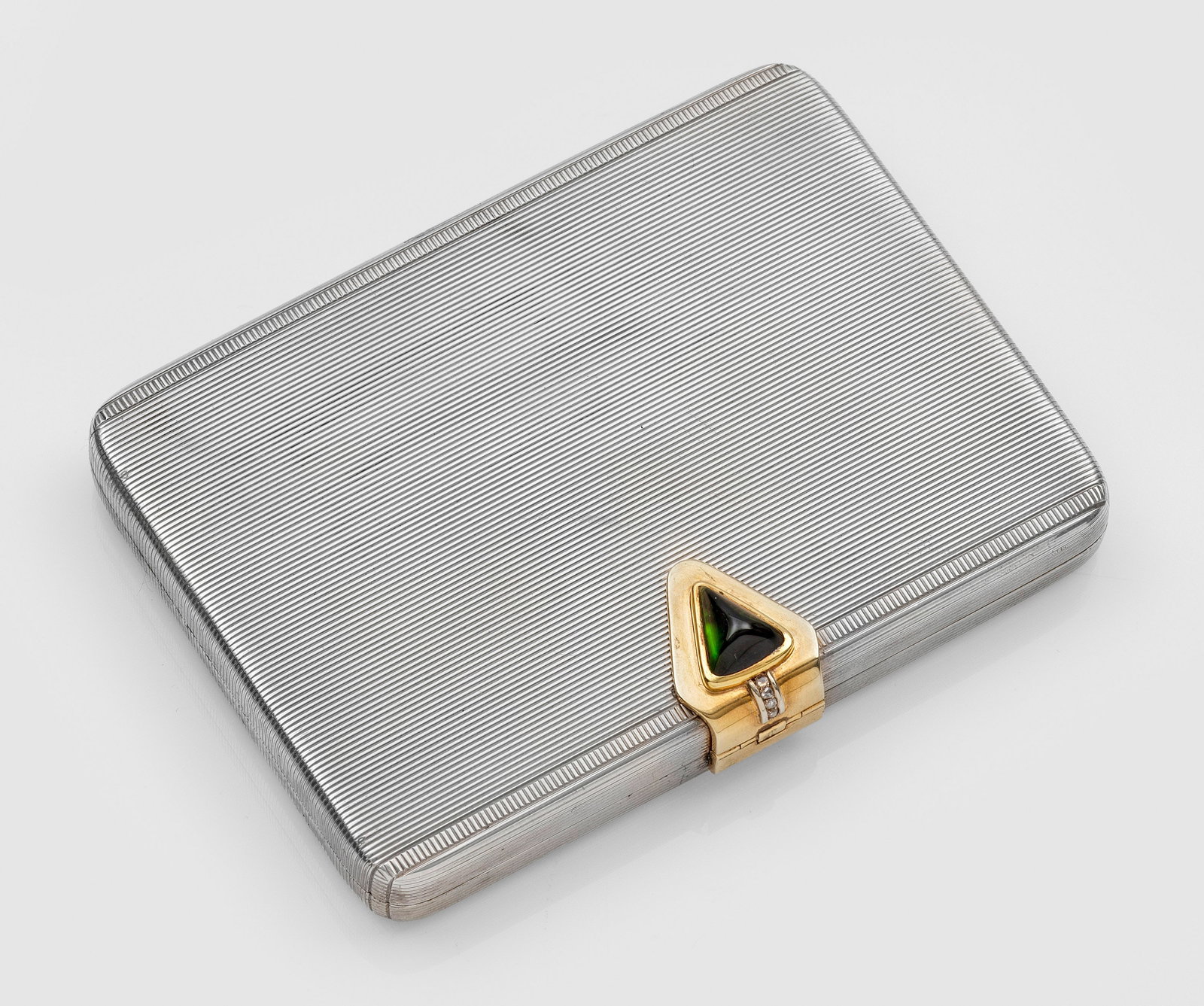 Art Déco-Schminketui: Sterlingsilber, teilw. vergoldet. Rechteckig mit gerundeten Ecken, flachem Scharnierdeckel und flächendeckendem Dekor aus feinen Rillen. Schauseitig mit grünem Stein besetzte Schließe. Im vergoldet