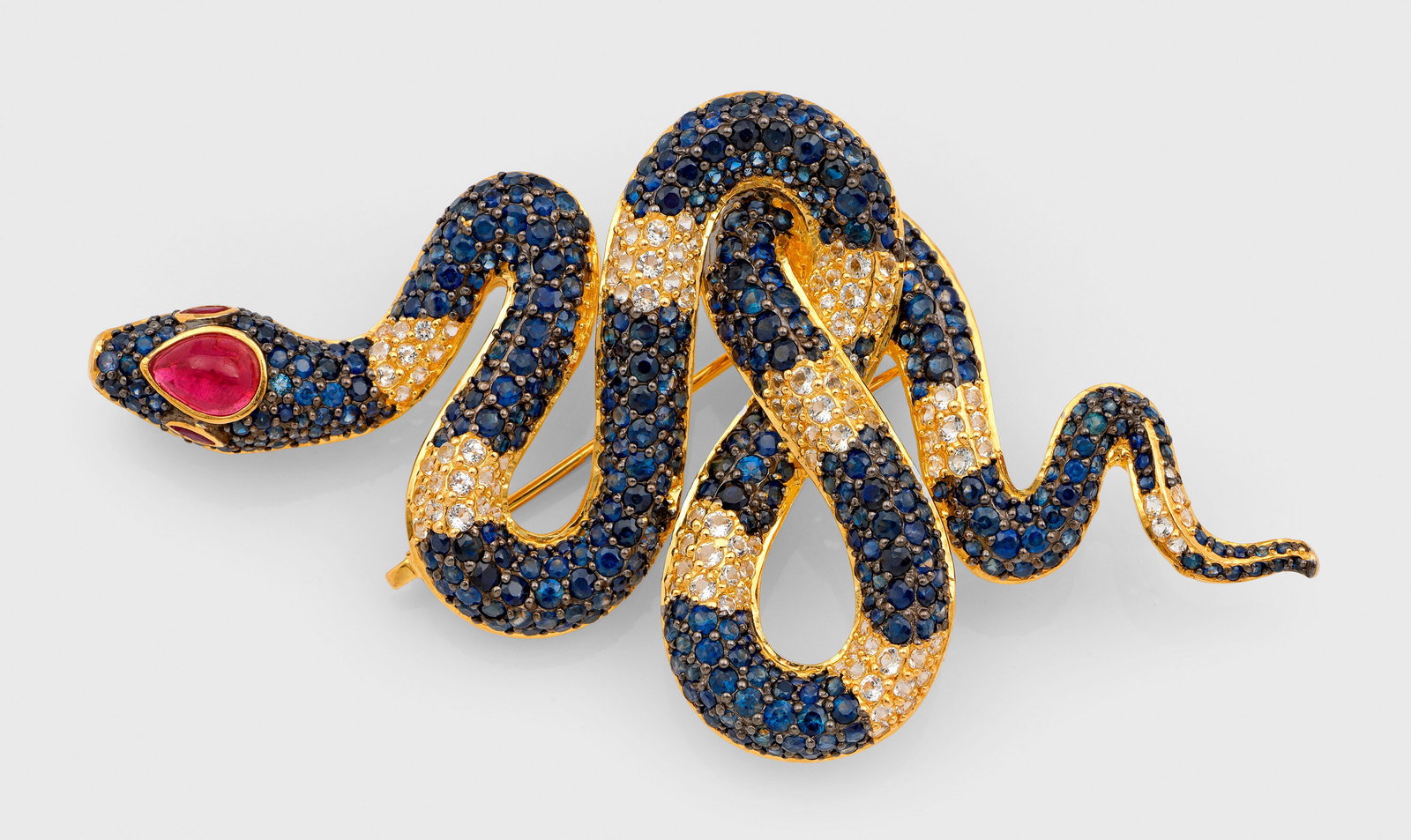 Dekorative Schlangenbrosche mit Saphiren und Rubin: Silber, vergoldet. Schauseitig besetzt mit nahezu kornblumenblauen und weißen Saphiren von zus. ca. 10 ct. in Pavéfassung und einem Rubincabochon. Gew. ca. 28,96 g. Brooch set with nearly cornflower