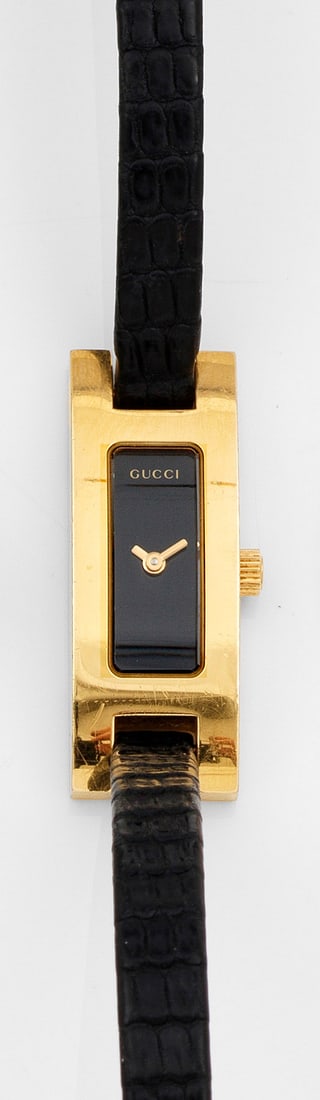 Damenarmbanduhr von GUCCI "Lady 3900L": Messing, vergoldet. Schmales, leicht bombiertes Uhrengehäuse, schwarzes Zifferblatt mit Stabzeiger. Schwarzes, geprägtes Lederarmband mit Gucci-Dornschließe. Quarzwerk. Herstellerzeichen. Ref.-Nr.
