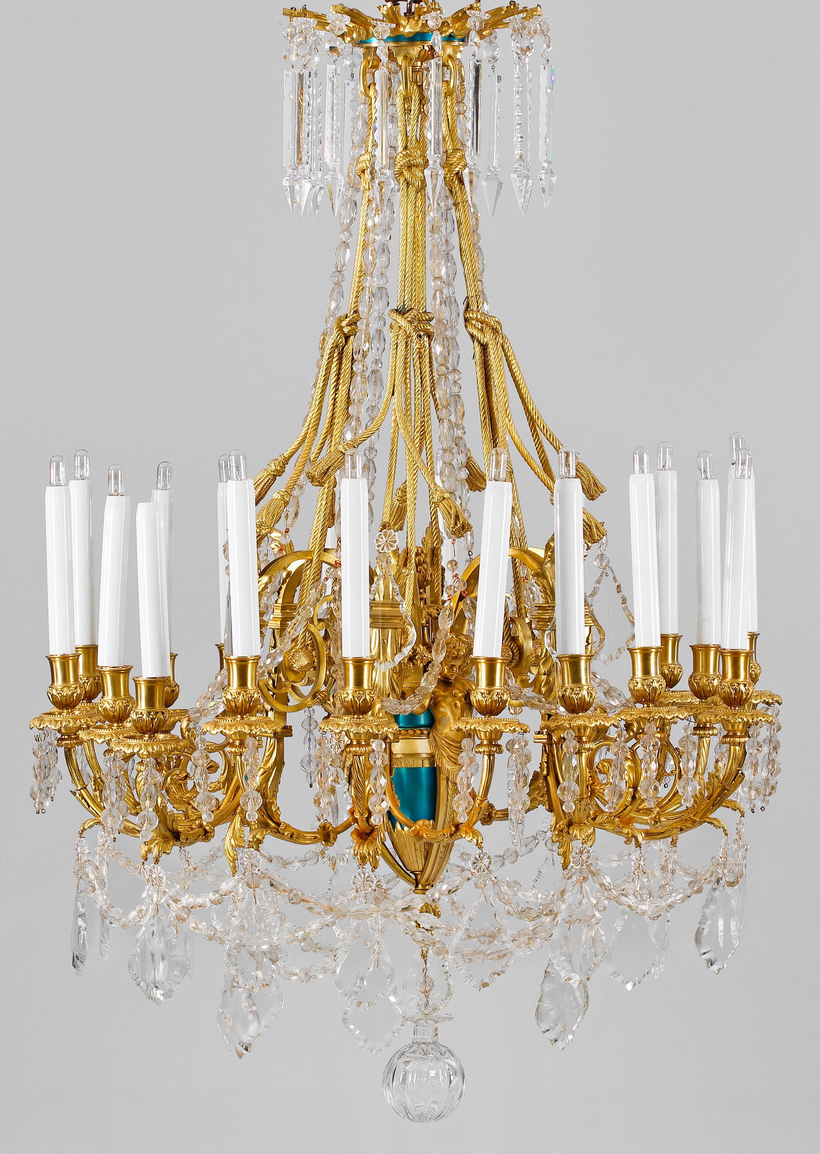 Großer Deckenlüster im Louis XVI-Stil: 18-flg.; Bronze, vergoldet und teilw. türkisfarben lackiert sowie farbloses Glas. Gegliederter Balusterschaft, flankiert von plastischen Genienfiguren als Träger für stark geschwungene, gekantete L
