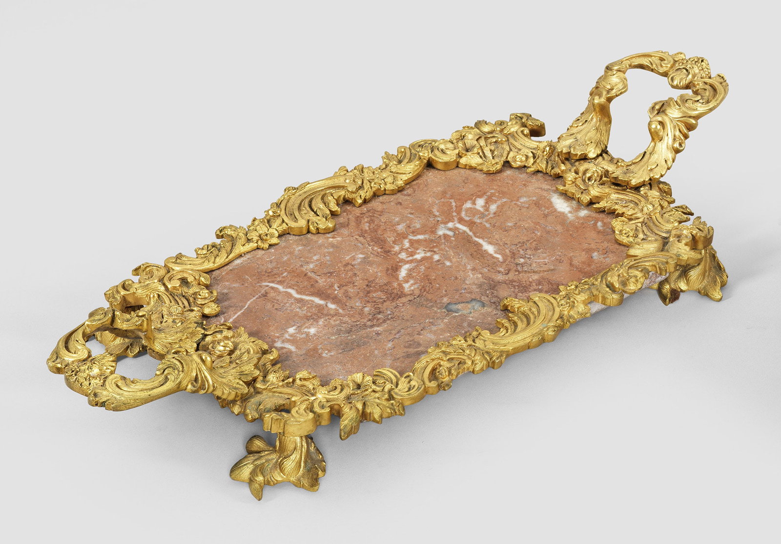 Louis Philippe-Prunktablett: Bronze, vergoldet sowie roséfarben gemaserter Marmor. Passig geschweifte Rahmung aus üppigen, gegeneinander gestellten Blattvoluten und Blüten, auf naturalistisch gestalteten Füßen. Korrespondier
