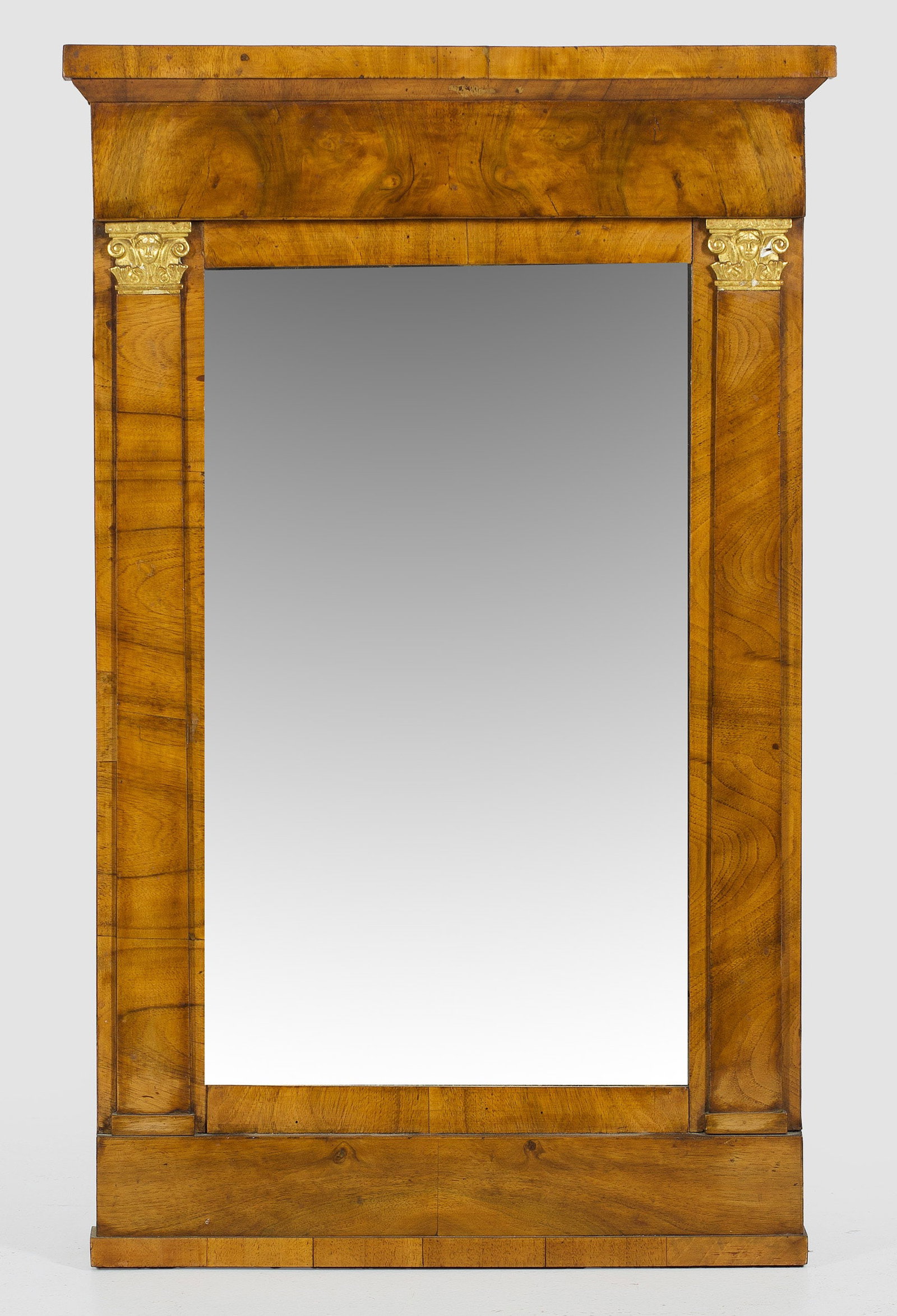 Biedermeier-Wandspiegel: Nussbaum, furniert sowie teilw. stuckiert und vergoldet. Gerade, hochrechteckige Spiegelrahmung, flankiert von flachen Pilastern mit korinthischen Kapitellen. Breites Giebelfeld sowie korrespondierend