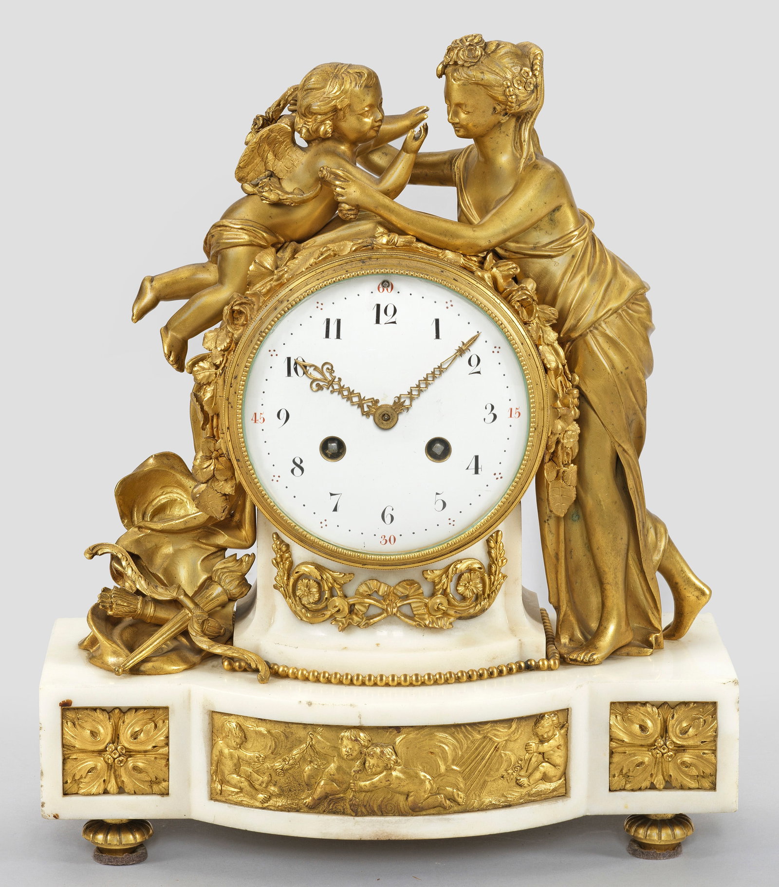 Louis XVI-Pendule "Amor und Venus": Weißer Marmor und Bronze, vergoldet. Querrechteckig angelegter, in der Front ausgebogter Sockel mit Puttenfries. Vollplastische Darstellung von Venus und Amor, auf das runde Uhrengehäuse gestützt.