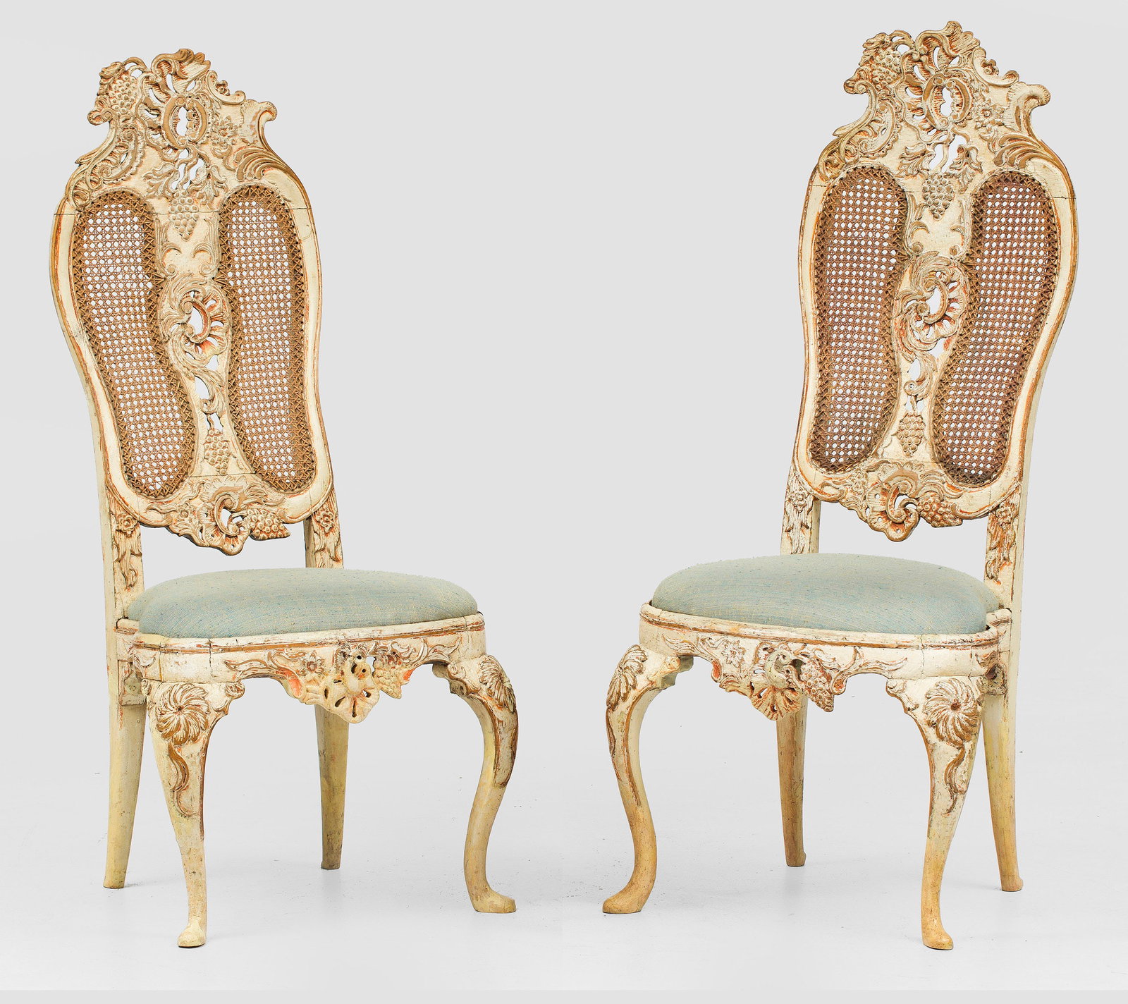 Paar Rokoko-Stühle: Holz, reliefplastisch geschnitzt und cremefarben gefasst. Bombierte Zarge auf stark geschwungenen Beinen. Hohe, passig geschweifte Rückenlehne mit asymmetrisch angelegter Bekrönung aus Rocaillen und