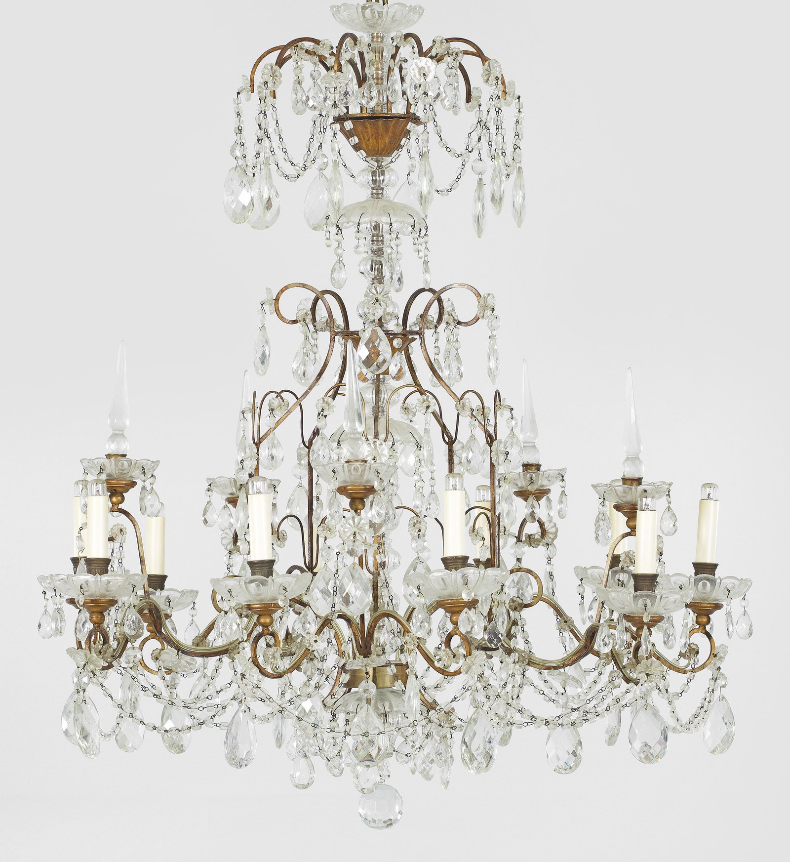 Großer Deckenlüster: 10-flg.; Metall, patiniert und farbloses Glas. Offen gestalteter Korpus aus stark geschwungenen, volutenförmig angelegten Streben als Träger für paarweise angeordnete Leuchtmittel mit großen Trauf