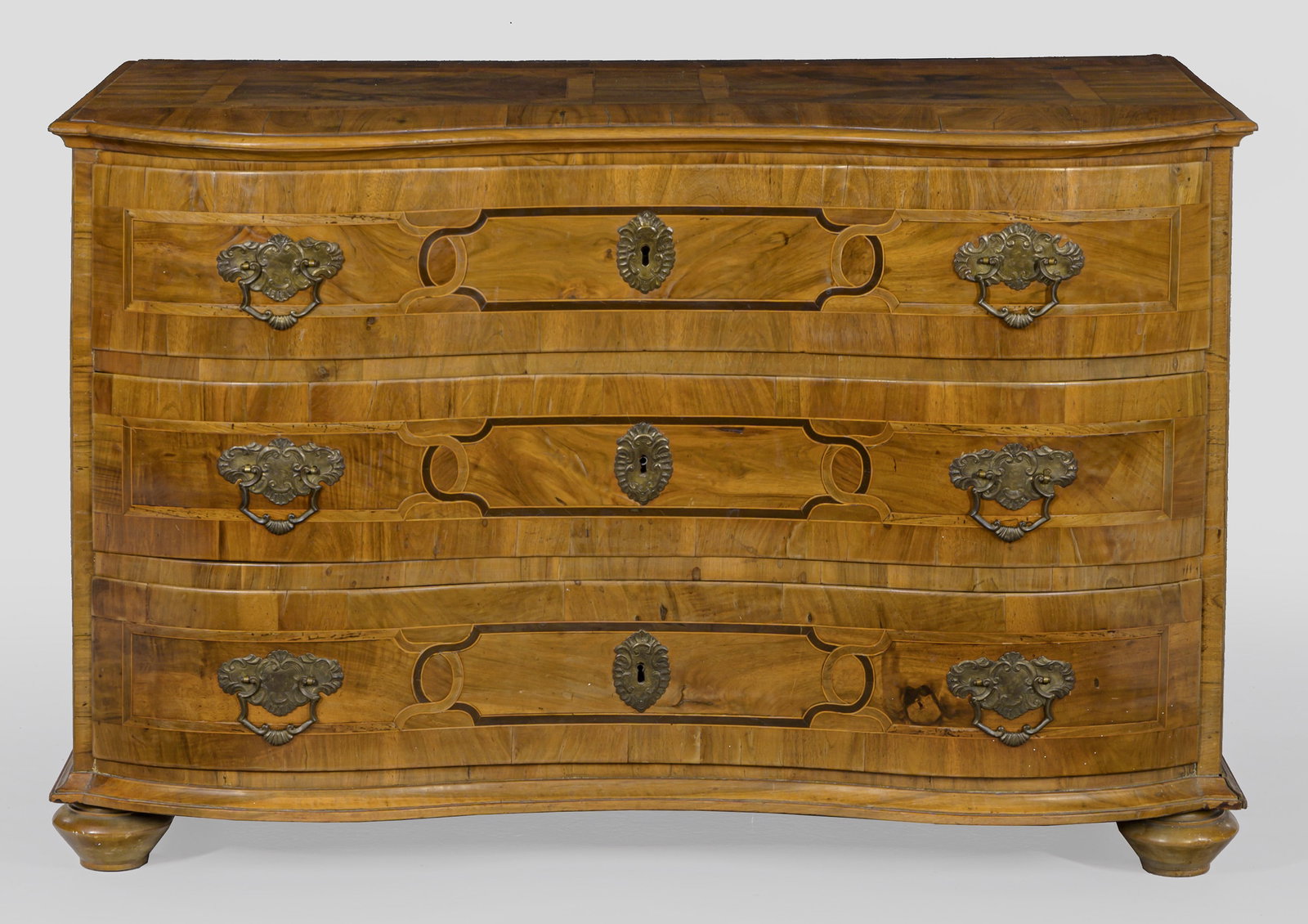 Barock-Kommode: Nussbaum, furniert. Gerader, querrechteckig angelegter Korpus auf schmaler Zarge und gedrückten Füßen. In der gegliederten Front drei breite, geschweifte Schubladen. Gering überstehende, profilier