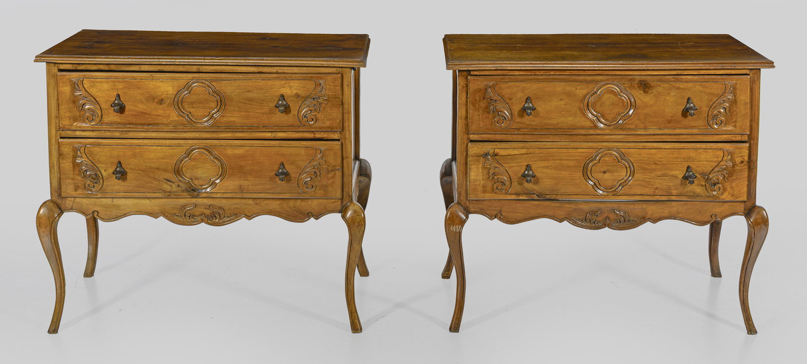 Paar Kommoden im Rokoko-Stil: Nussbaum, teilw. reliefplastisch geschnitzt. Gerader, querrechteckiger Korpus auf stark geschwungenen Beinen. In der gegliederten Front zwei breite Schubladen. Gering überstehende, profilierte Deckpl