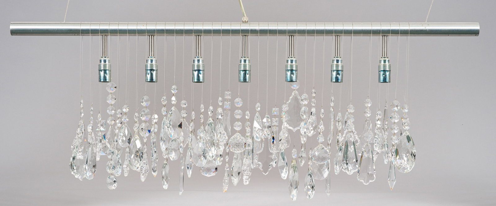 Pendelleuchte "Cellula": 7-flg.; Aluminium und farbloses Kristallglas. Quergelegter Rundschaft als Träger für Leuchtmittel. Üppiger Behang aus asymmetrisch angeordneten unterschiedlichen Prismen. Elektrifiziert. Entw. Nunz
