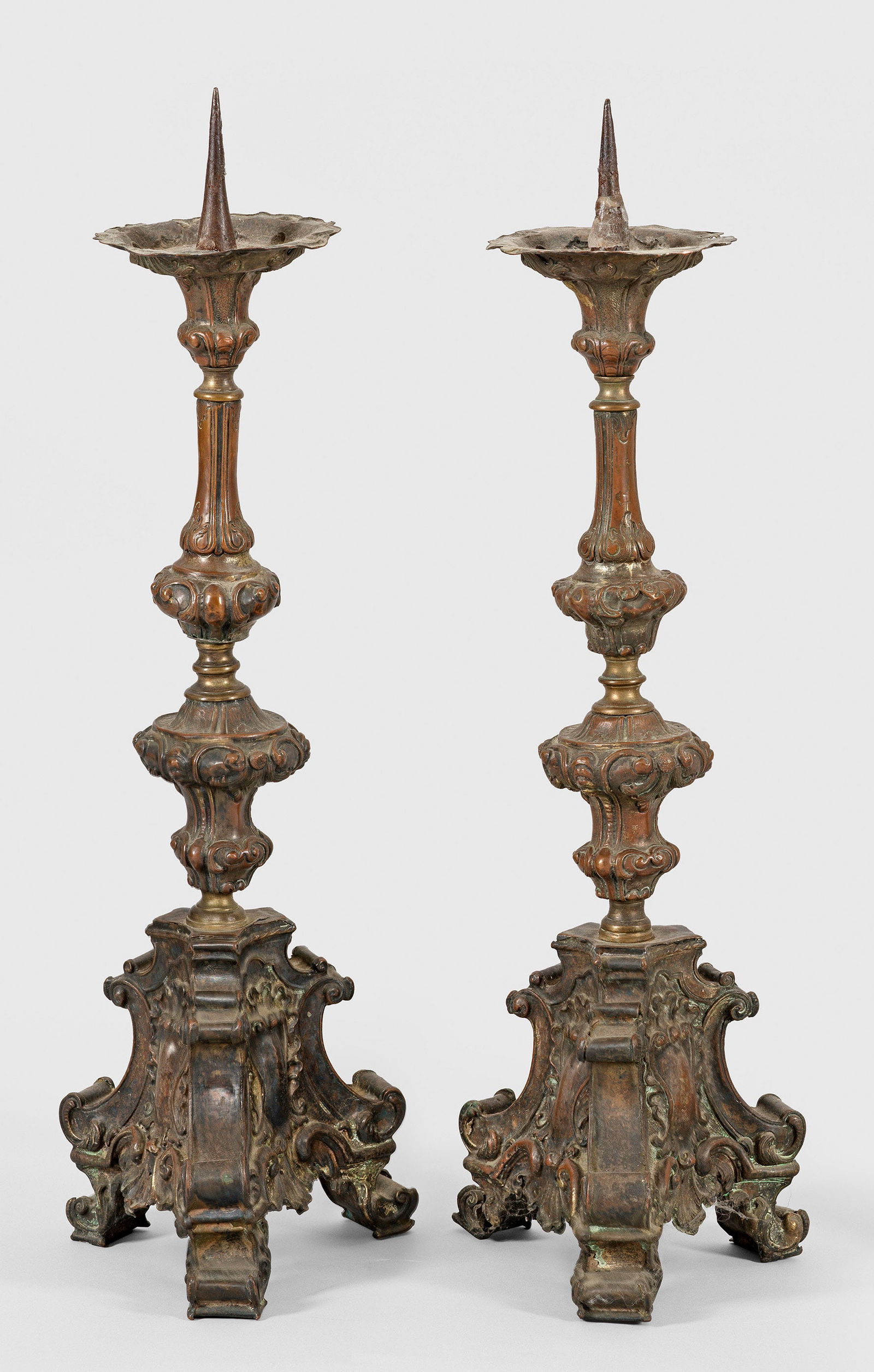 Paar Kerzenleuchter im Barock-Stil: 1-flg.; Kupfer und Messing, patiniert. Über geschweift ansteigender Basis mit Kartuschenmotiven mehrfach gegliederter Balusterschaft als Träger für Leuchtmittel mit großem Dorn. Besch.; H. 54 cm.