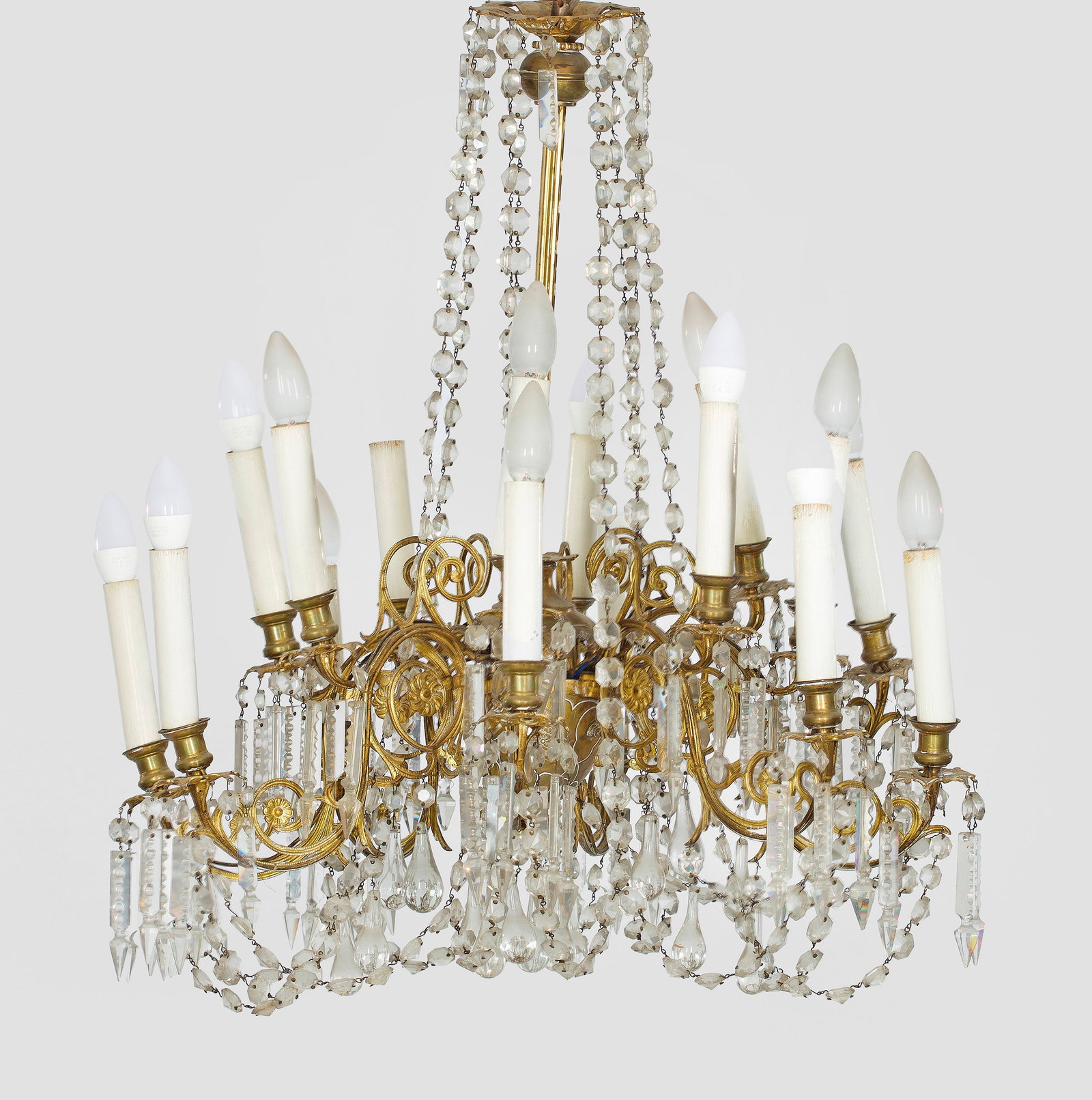 Belle Epoque-Deckenlüster: 16-flg.; Metall und farbloses Glas. Schlanker Schaft. Unterhalb davon ausgehend stark geschwungene Leuchterarme als Träger für gestuft angeordnete Leuchtmittel. Reicher Behang aus facettierten Prism