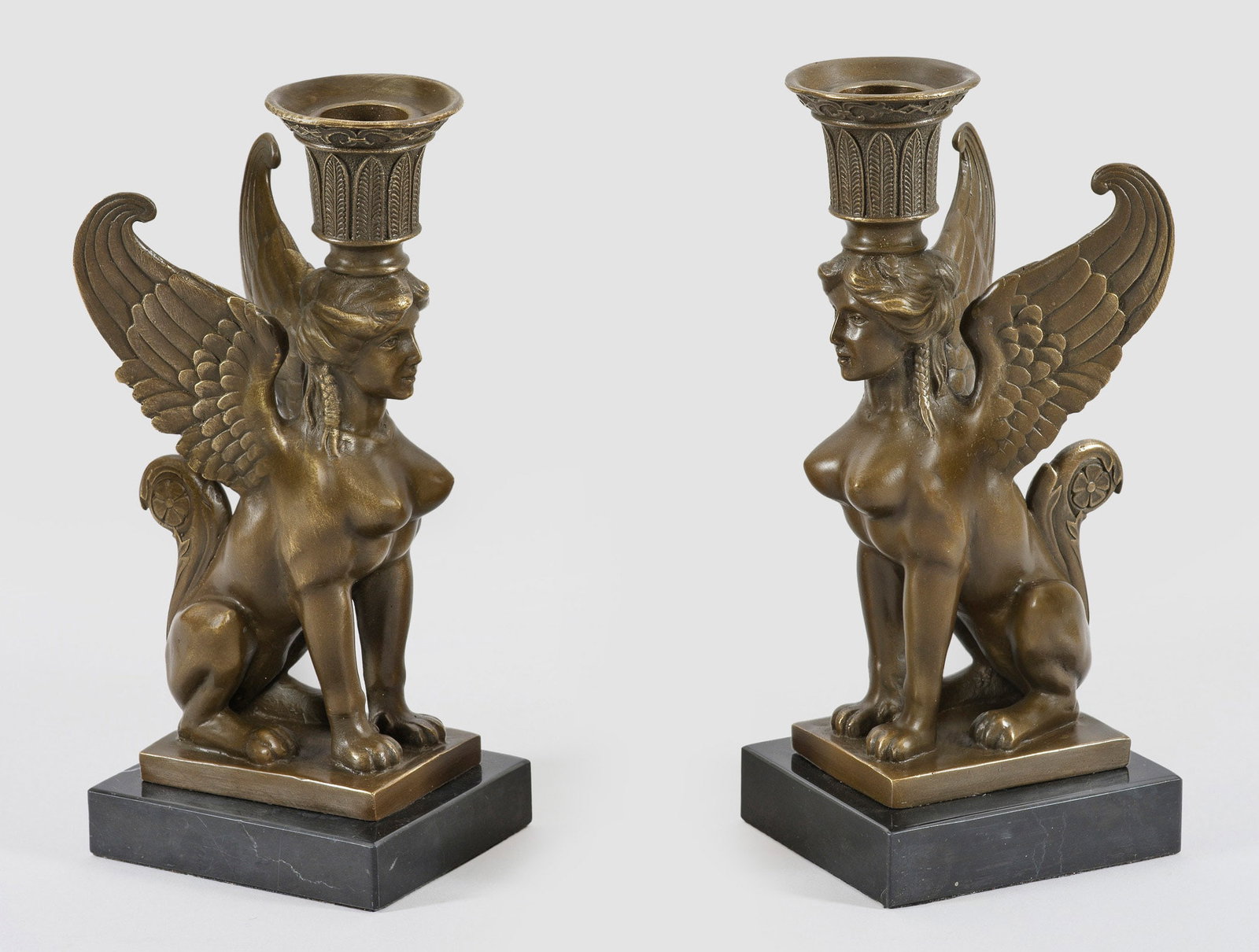 Paar Leuchter im Empire-Stil: Bronze, patiniert und schwarzer Marmor. Über rechteckiger Basis vollplastisch gestaltete Sphinxen als Träger für Leuchtmittel, in Form einer mit Lanzettblättern dekorierten Kerzentülle. H. 23 cm.