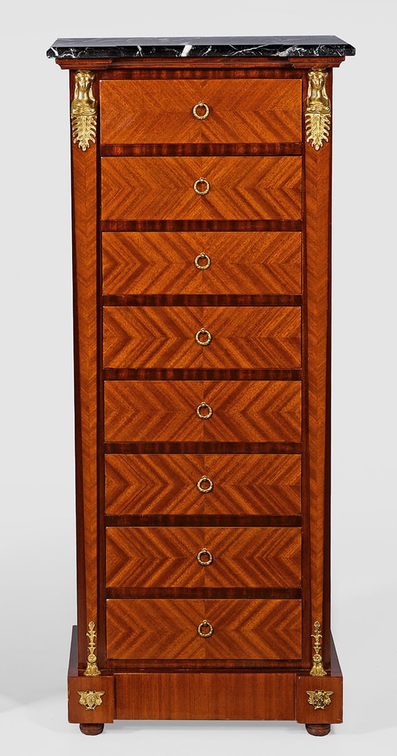 Chiffonière im Empire-Stil: Mahagoni, furniert. Gerader, hochrechteckiger Korpus auf gekantetem Sockel. In der gegliederten Front acht Schubladen, flankiert von eingestellten Karyatiden. Deckplatte aus grau-weiß gemasertem Marm