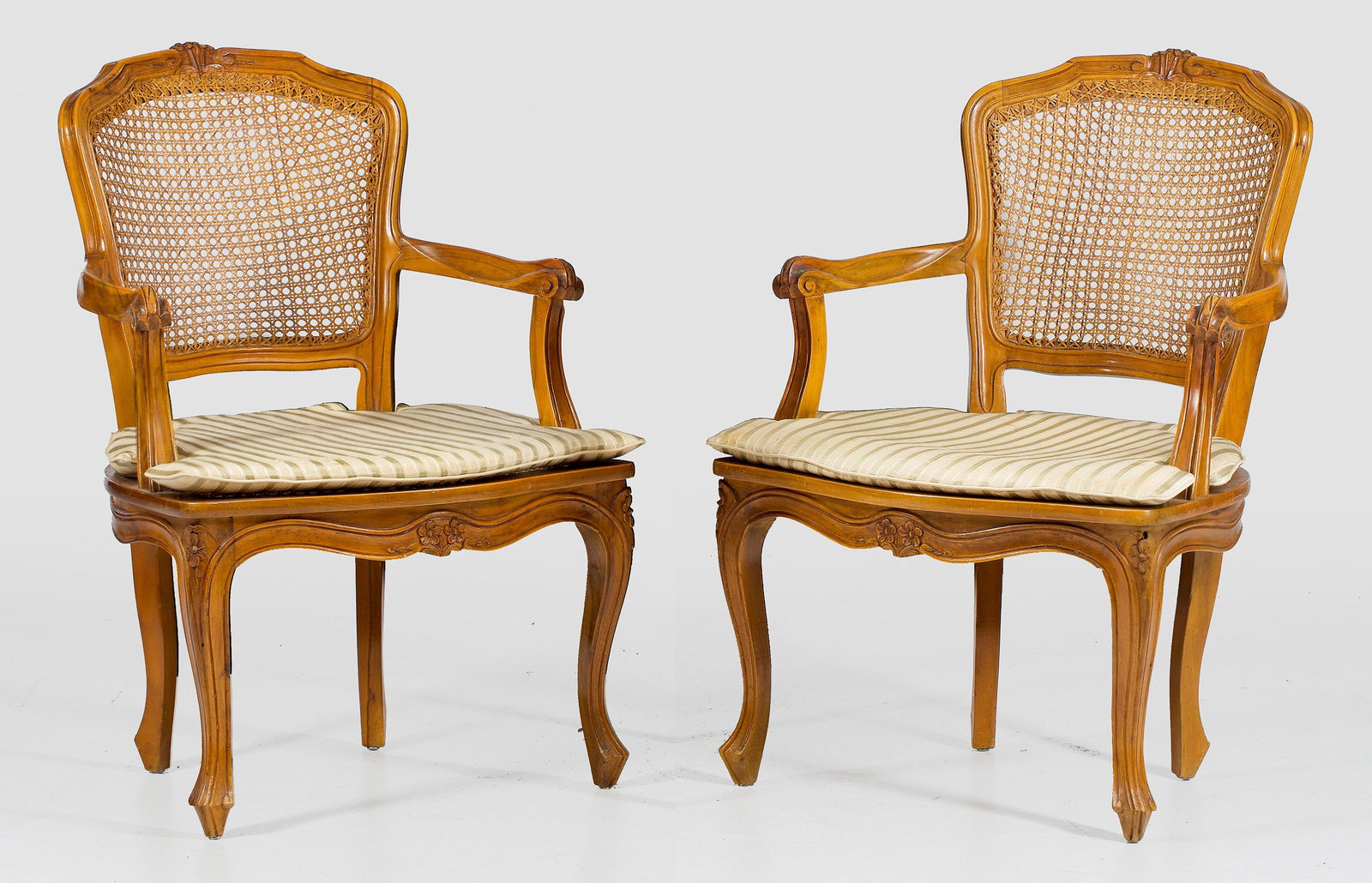 Paar Armlehnstühle im Louis XV-Stil: Nussbaum, teilw. reliefplastisch geschnitzt. Passig geschweifte Zarge auf geschwungenen Beinen, gebogte Stützen für schmale Armlehnen sowie schildförmige Rückenlehnenrahmung. Sitz- und Lehnenfläc