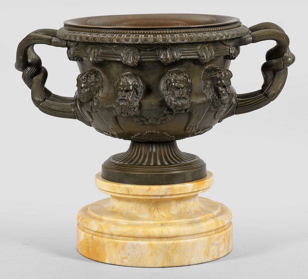 Warwick-Vase als Grand Tour-Objekt: Bronze, dunkel patiniert sowie gelb gemaserter Marmor. Über gestuft ansteigendem Profilsockel balusterförmiger, teilw. kannelierter Korpus nach dem Vorbild der berühmten 1771 wieder entdeckten