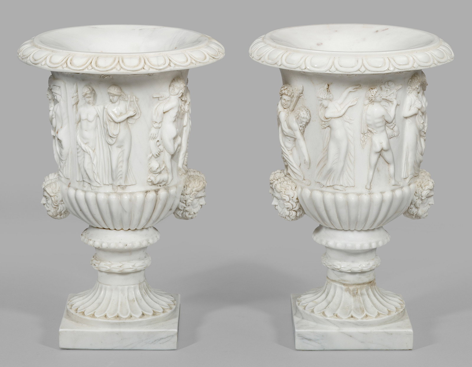 Paar Borghese-Vasen: Weißer, cremefarben gemaserter Marmor. Über quadratischer Plinthe kraterförmiger, teilw. godronierter Korpus mit breitem Lippenrand aus Eierstabfries. Umlaufend der Wandung erhaben reliefierte Dars