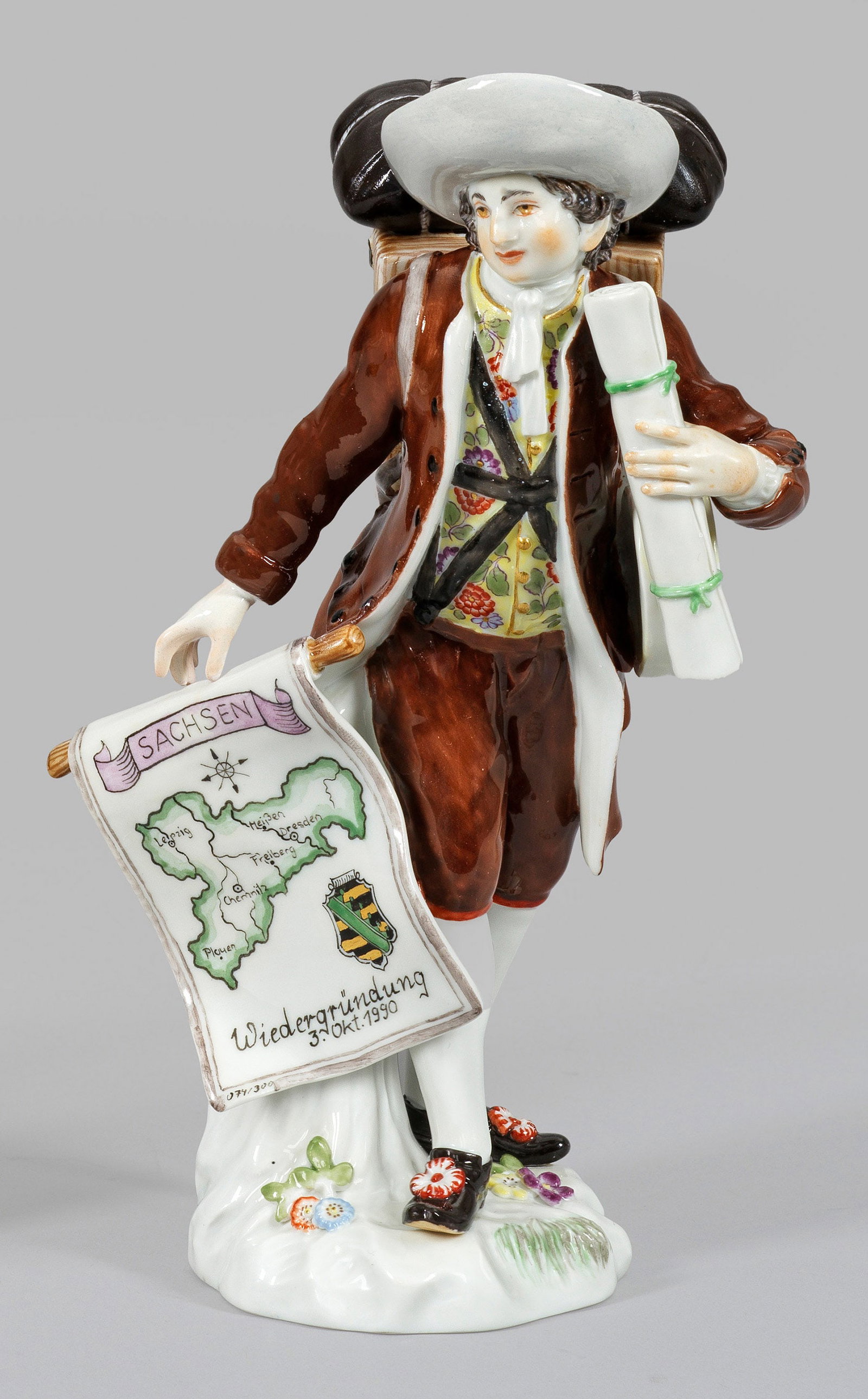 Landkartenverkäufer: aus der Serie „Cris de Paris“. Auf einem mit plastischen Blüten und Blättern belegtem Natursockel stehender Kartenhändler, bepackt mit einer Transportkiste und Karten, zu seiner Rechten ein Ban