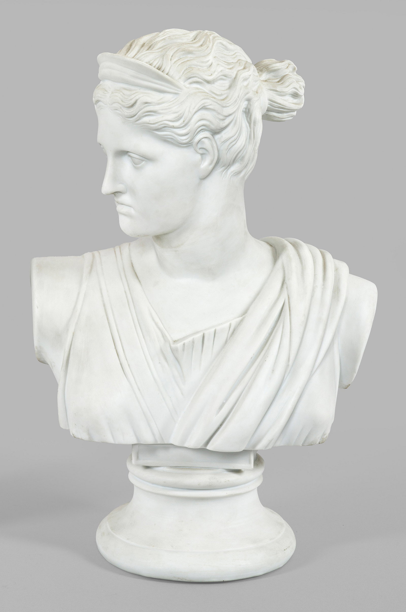 Diana-Büste: Biskuitporzellan. Über eingezogenem Rundsockel die Büste, der nach rechts gewandten Jagdgöttin, gestaltet in Anlehnung an die Diana von Versailles aus dem Louvre. Manufakturmarke. H. 43,5 cm. A bis
