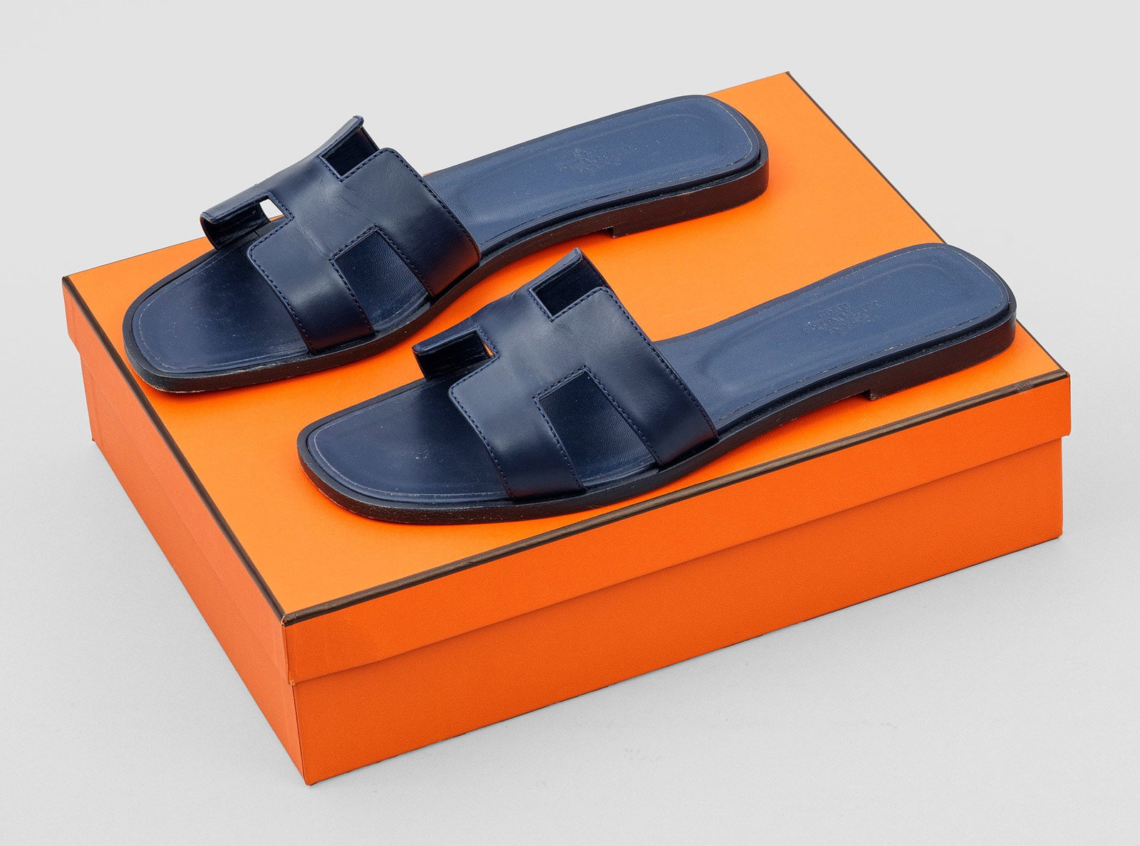 Paar Damen-Sandalen "Oran" von HERMÈS: Indigoblaues Leder. Flache Sandale mit breitem Riegel aus stilisiertem H-Logo. Gr. 38,5. Wenig getragen. Original Box und Staubbeutel. A pair of pre-owned indigo blue leather sandals by HERMÈS. Rarel