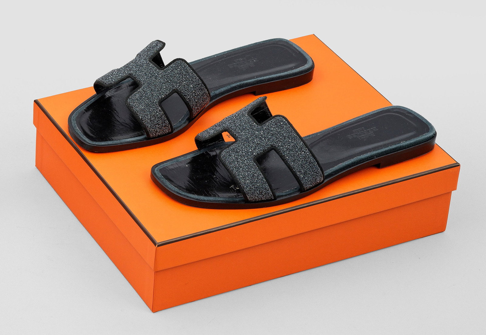 Paar Damen-Sandalen "Oran" von HERMÈS: Pudre de Christal und schwarzes Leder. Flache Sandale mit breitem Riegel aus stilisiertem H-Logo. Gr. 38,5. Getragen. Original Box und Staubbeutel. A pair of pre-owned poudre de cristal and black leat