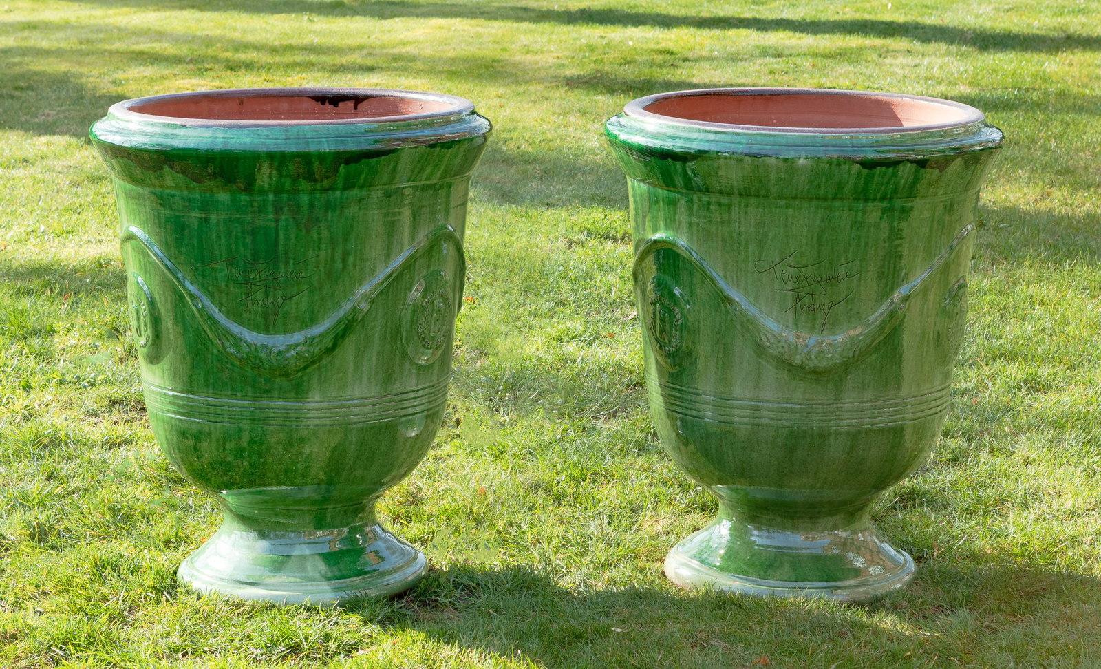 Paar große Pflanzgefäße: Terrakotta, grün glasiert. Über profilierter Basis sich weitender, kelchförmiger Korpus mit breitem, leicht vorkragendem Lippenrand. Umlaufend der Wandung erhaben reliefierte, stilisierte Festons.