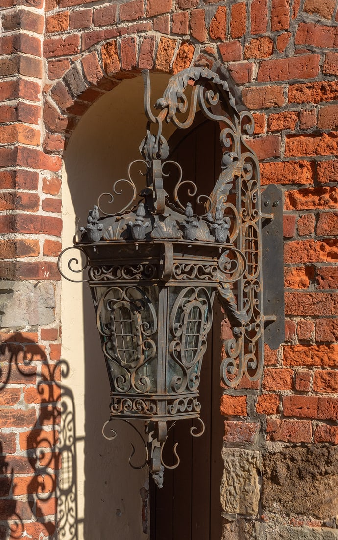 Paar große Wandlaternen im Barockstil: 1-flg.; Schmiedeeisen. Balusterförmiger, sich konisch weitender Korpus aus volutenartig angelegten Stegen mit Glaseinsätzen sowie flacher, kuppelförmiger oberer Abschluss mit Balusterbekrönungen.