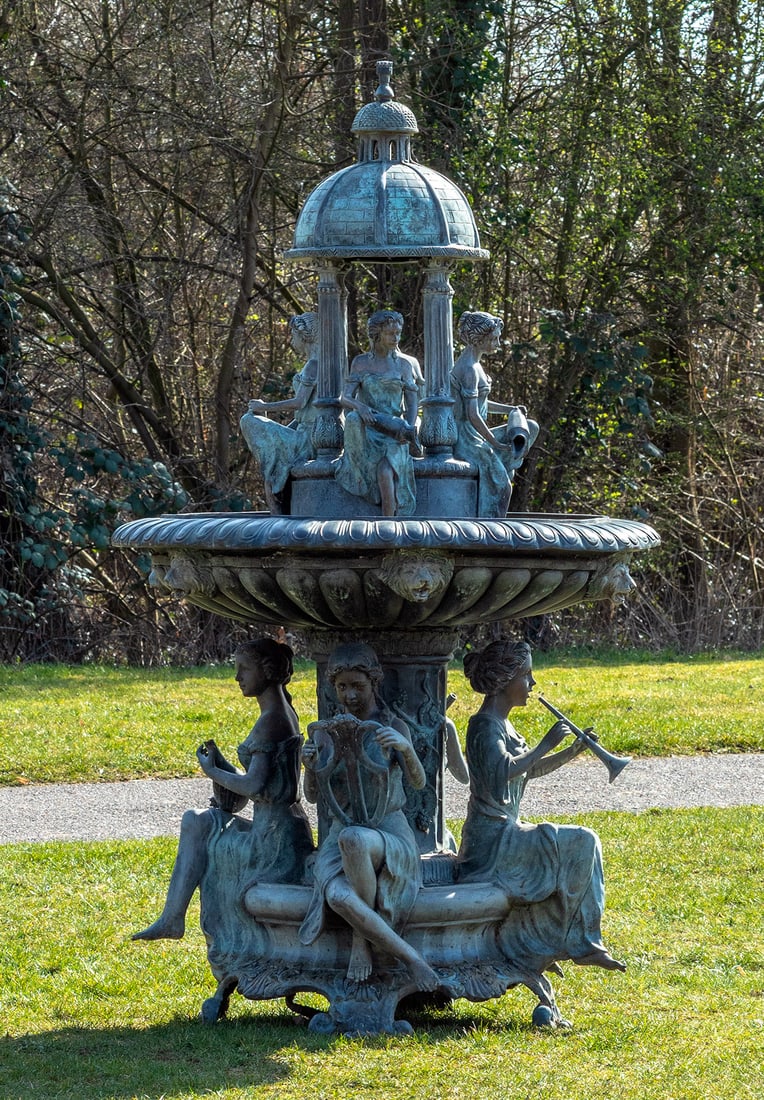 Großer repräsentativer Pakbrunnen im Belle Epoque-Stil: Bronze, patiniert. Über geschweift ansteigender Basis, zylinderförmiger, kannelierter Schaft mit reliefierten Weinreben, umgeben von vollplastisch gestalteten musizierenden Kinderfiguren als Träger