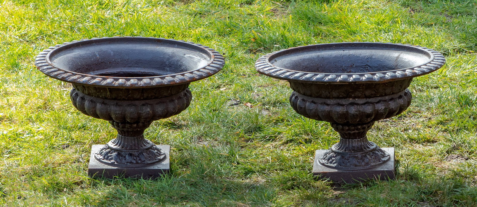 Paar Gartenvasen: Gusseisen, braun lackiert. Über quadratischer Plinthe flacher, umlaufend godronierter Korpus mit weit vorkragendem Lippenrand aus Eierstabfries. H. 30 cm. A pair of French brown lacquered iron garden
