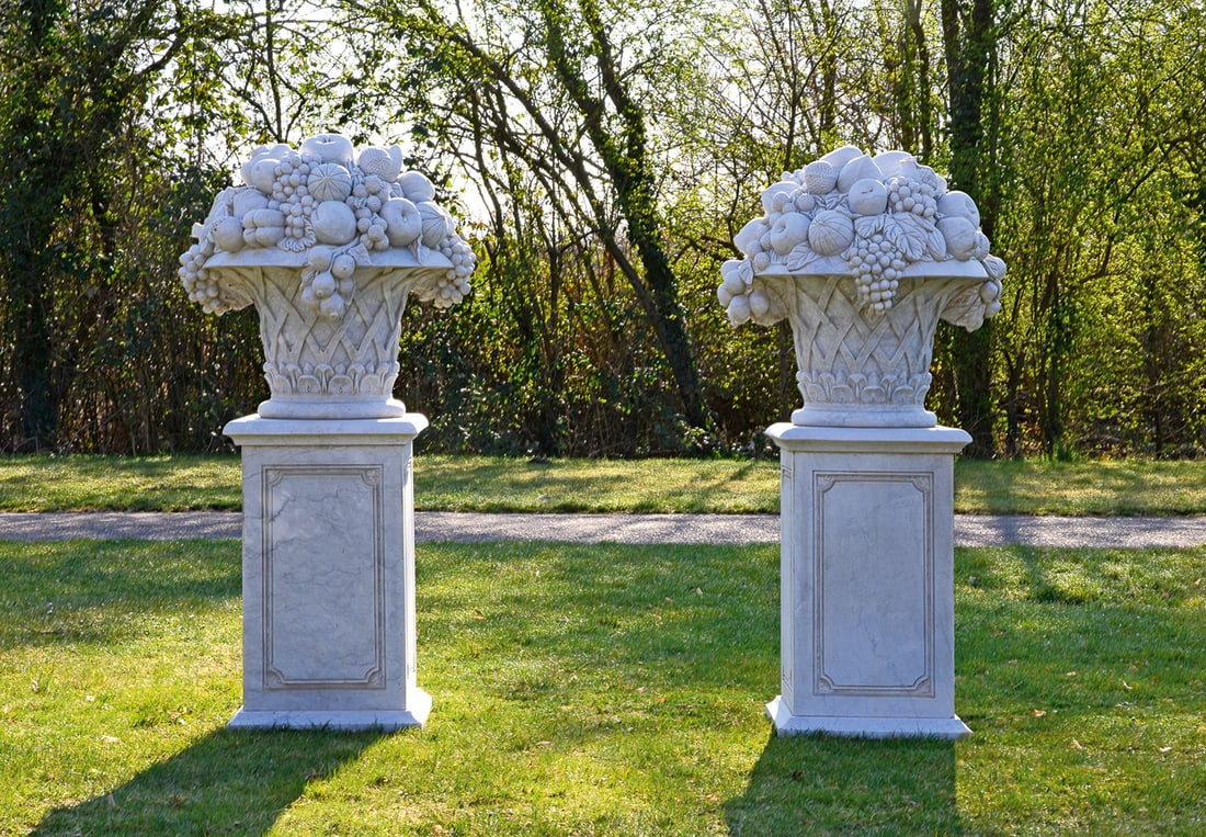Paar große repräsentative Parkdekorationen im Louis XVI-Stil: Weißer, hellgrau gemaserter Marmor. Über hohem, allseitig kassettiertem Podestsockel auf schmaler, gekehlter Basis große, plastisch gestaltete Dekorationen in Form von kraterförmigen Körben aus r