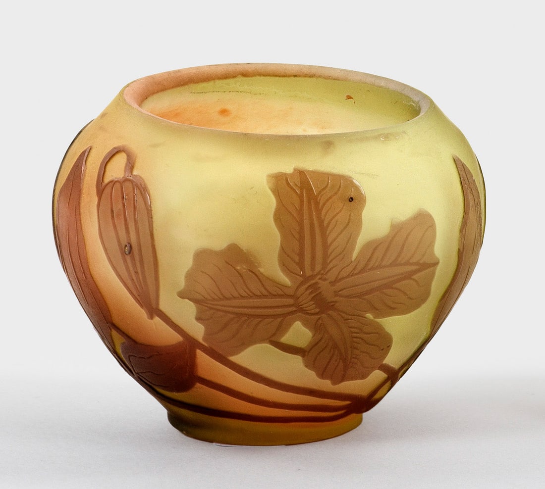 Kleine Gallé-Ziervase mit Clematis-Dekor: Gedrückt-ovoide Form mit weiter Mündung. Überfangglas, farblos, weiß, gelblich und violett. In mehreren Arbeitsgängen geätzter Dekor. Sign. "Gallé". H. 5,2 cm. A French Art Nouveau cameo glass 
