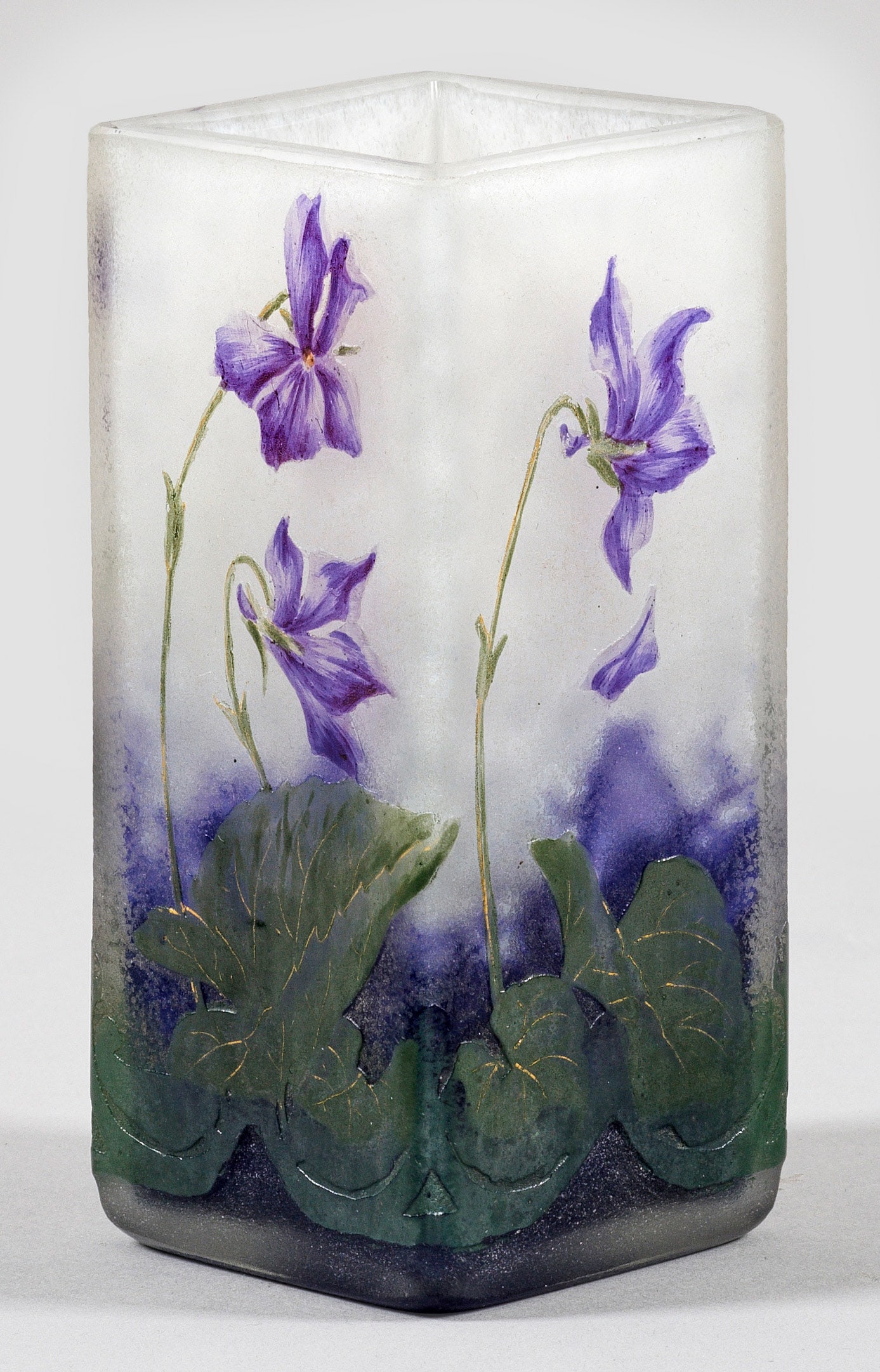 Jugendstil-Ziervase mit Veilchen-Dekor von Daum Frères: Becherform, quadratischer Querschnitt. Überfangglas, farblos, mit flockigen, weißen und dichten violetten Pulvereinschlüssen. Umlaufender Dekor aus blühenden Veilchen, am Ansatz ornamentales Band,