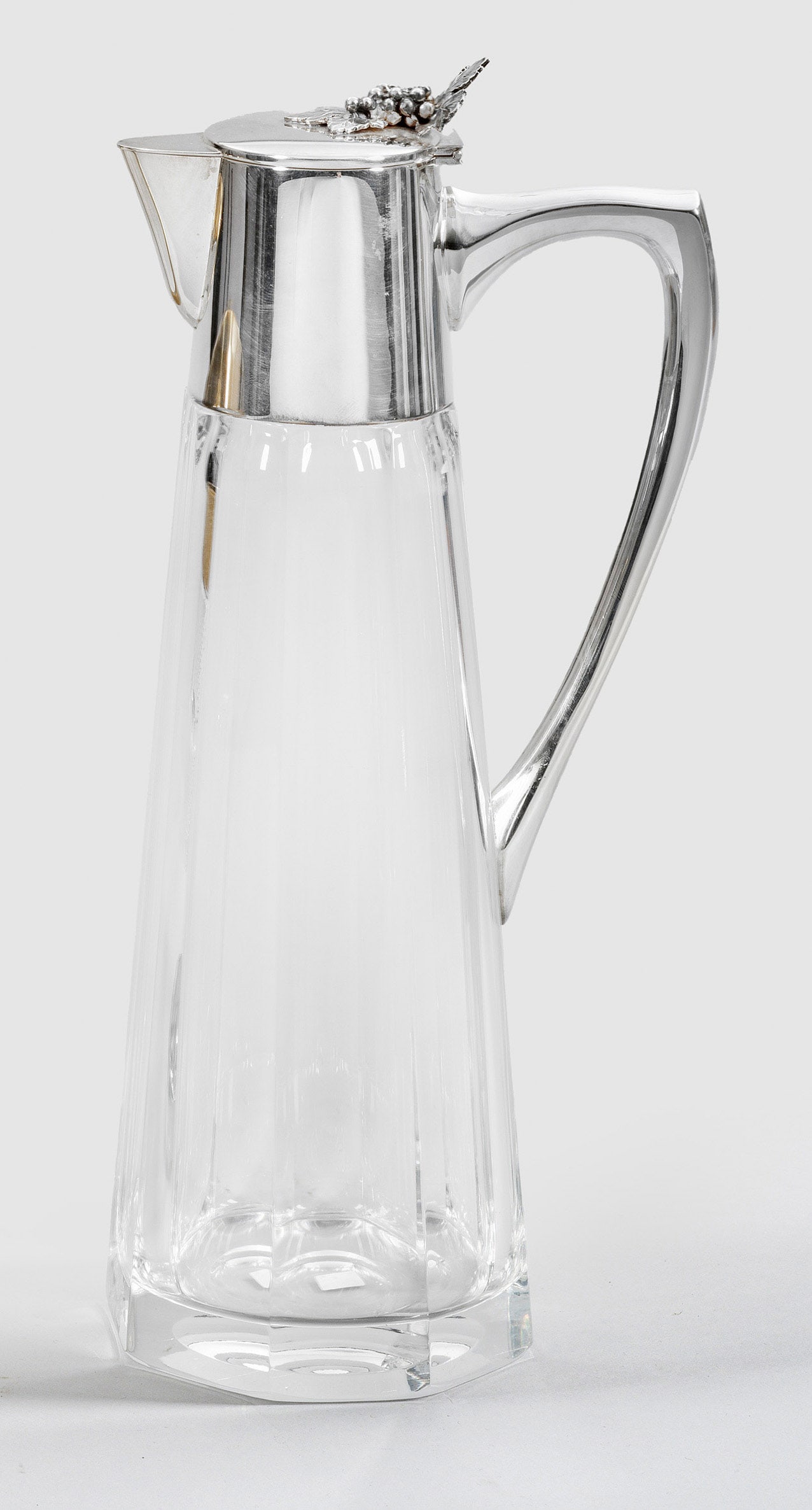 Art Déco-Weinkaraffe: mit Sterlingsilbermontierung. Achtfach gekanteter, konischer Korpus aus farblosem Glas. Glatte Silbermontierung mit rückseitigem Henkel, kurzem Konsolausguss und gering aufgewölbtem Scharnierdeckel 