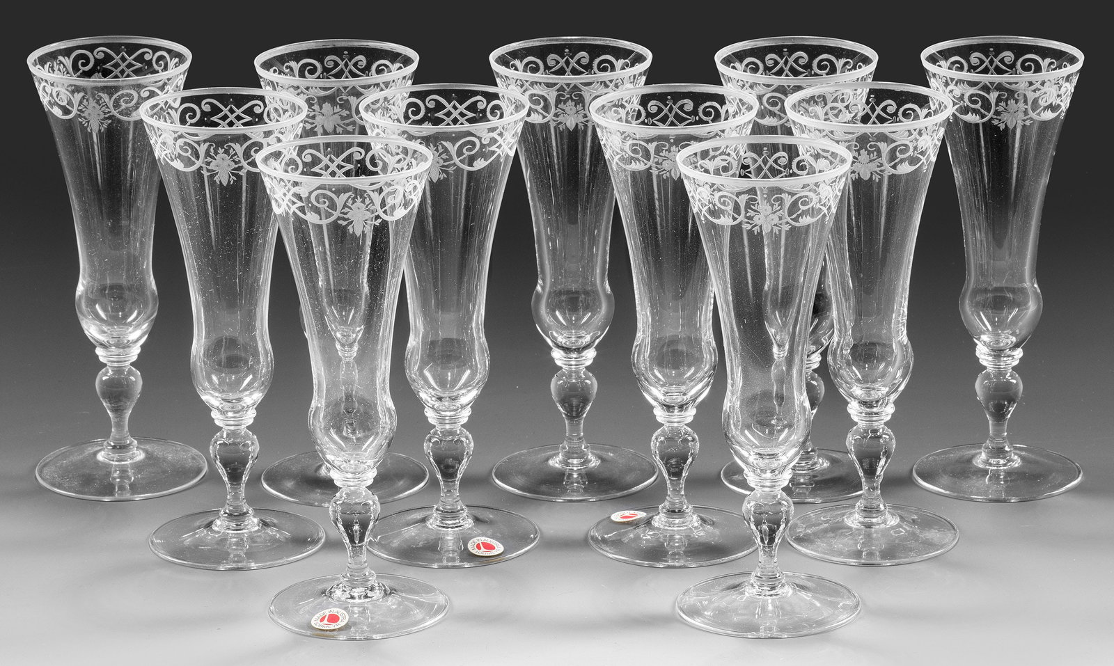 11 Lobmeyr-Champagnerflöten aus dem Trinkservice "Barock": Farbloses Kristallglas. Sog. "Champagner hoch". Flacher Scheibenfuß, Balusterschaft, glockenförmige Kuppa. Geschnittene Bandelwerkbordüre. Entw. Stefan Rath 1905. Jeweils Firmen-Monogramm, zwei Gl�