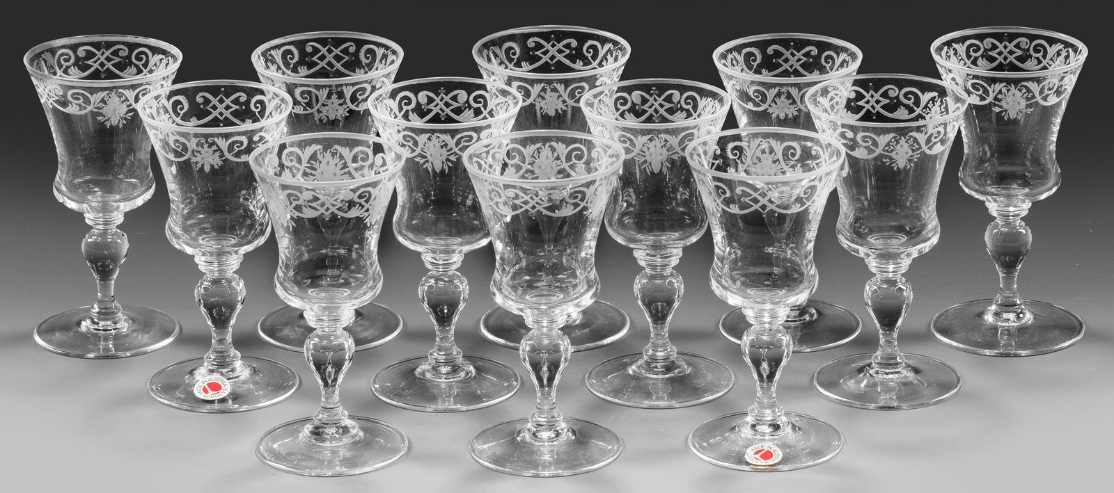 12 Lobmeyr-Sherrygläser aus dem Trinkservice "Barock": Farbloses Kristallglas. Flacher Scheibenfuß, Balusterschaft, glockenförmige Kuppa. Geschnittene Bandelwerkbordüre. Entw. Stefan Rath 1905. Jeweils Firmen-Monogramm, zwei Gläser mit Etikett "LOBMEY