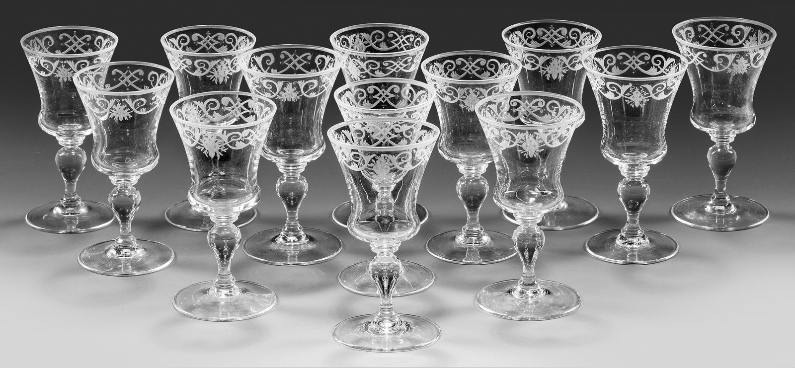 13 Lobmeyr-Sherrygläser aus dem Trinkservice "Barock": Farbloses Kristallglas. Flacher Scheibenfuß, Balusterschaft, glockenförmige Kuppa. Geschnittene Bandelwerkbordüre. Entw. Stefan Rath 1905. Jeweils Firmen-Monogramm. H. 12,3 cm. Inspiriert durch ein