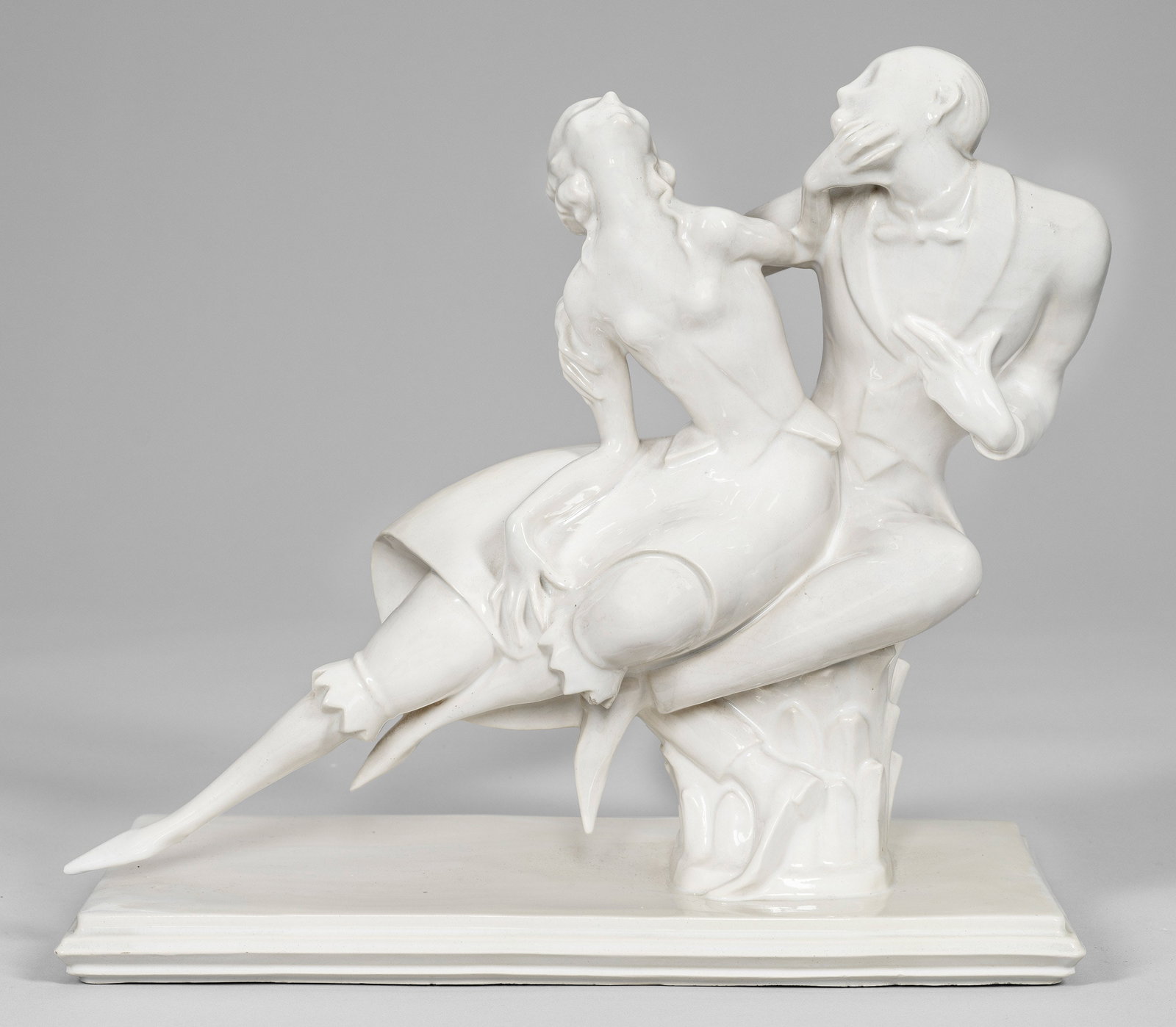Art Déco-Tanzgruppe: Fayence, altweiß glasiert. Auf profilierter Rechtecksplinthe Dame und Herr in eng verschlungener Tanzpose. Entw. Emil Sutor. Geprägte Manufakturmarke. Unw. rest.; H. 30,5 cm x 34 cm x 17,5 cm. Ein V