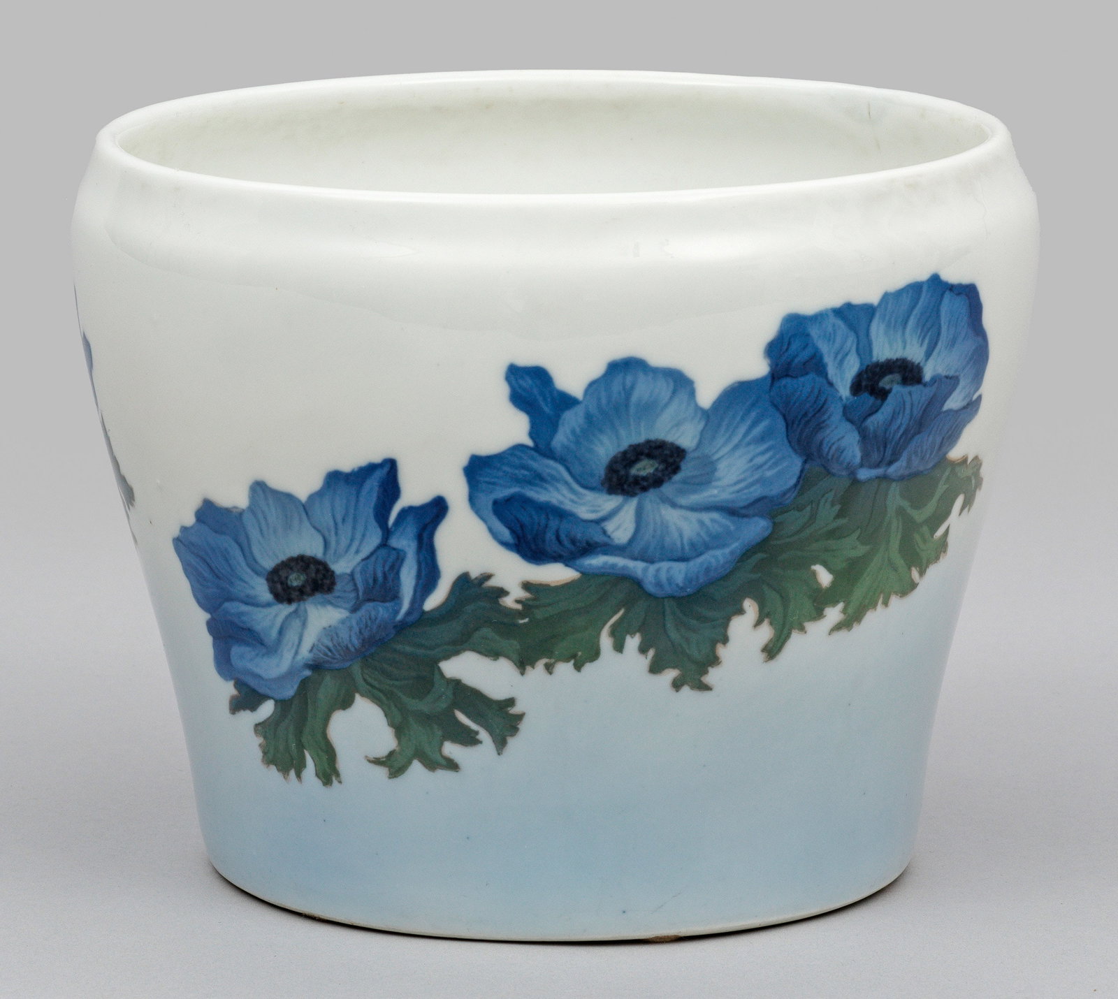 Cachepot mit Blumendekor: Walzenfömig sich erweiternder Korpus mit kurz eingezogenem Rand. Über zartblauem Fond umlaufende Mohnblüten in polychromer Unterglasurmalerei. Manufakturamrke. H. 17 cm. A porcelain cachepot with f